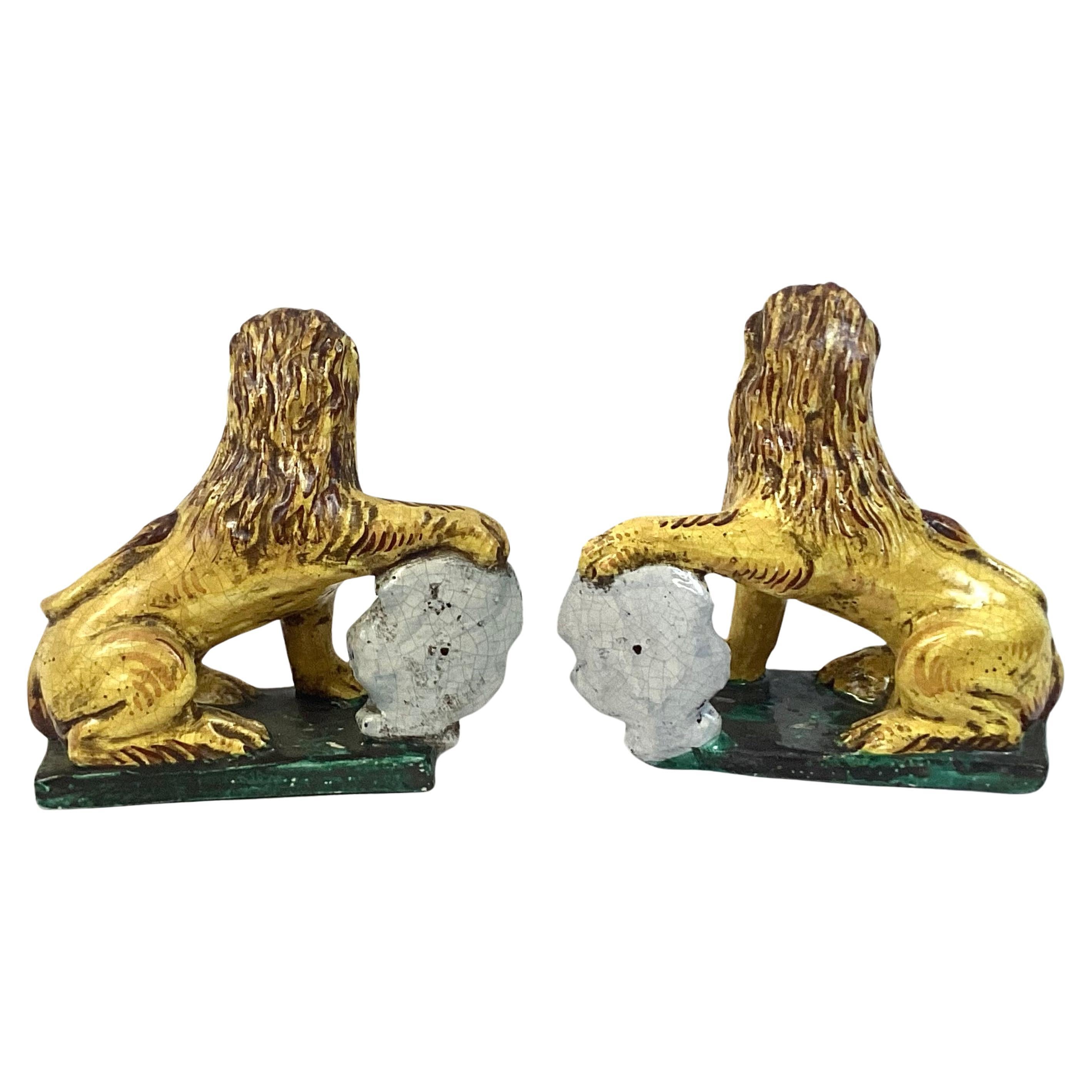 Pareja de leones de loza italiana de principios del siglo XX con escudos de armas. Leones amarillos y marrones pintados a mano, escudos azules, rojos y blancos y base verde. 