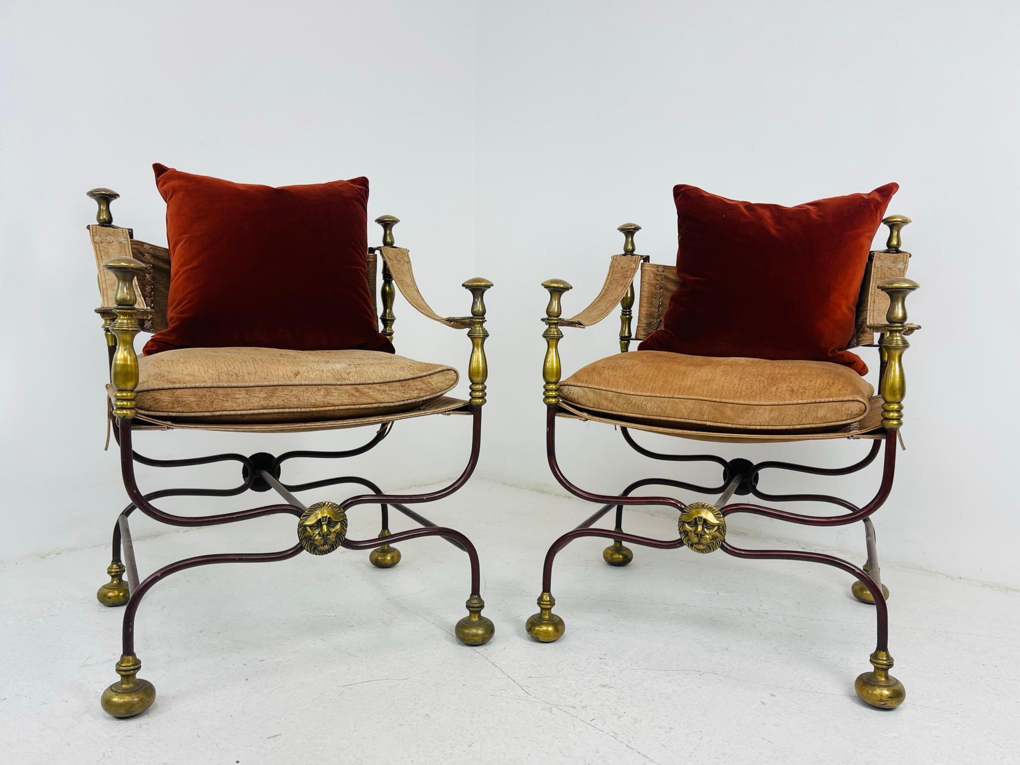 Pair of early 20th century campaign chairs with leather seats, arms and back. Chairs feature wrought iron bases leading to bronze details and feet. Bronze lion medallions adorn the intersection at the front and backside of the chairs. Regal yet