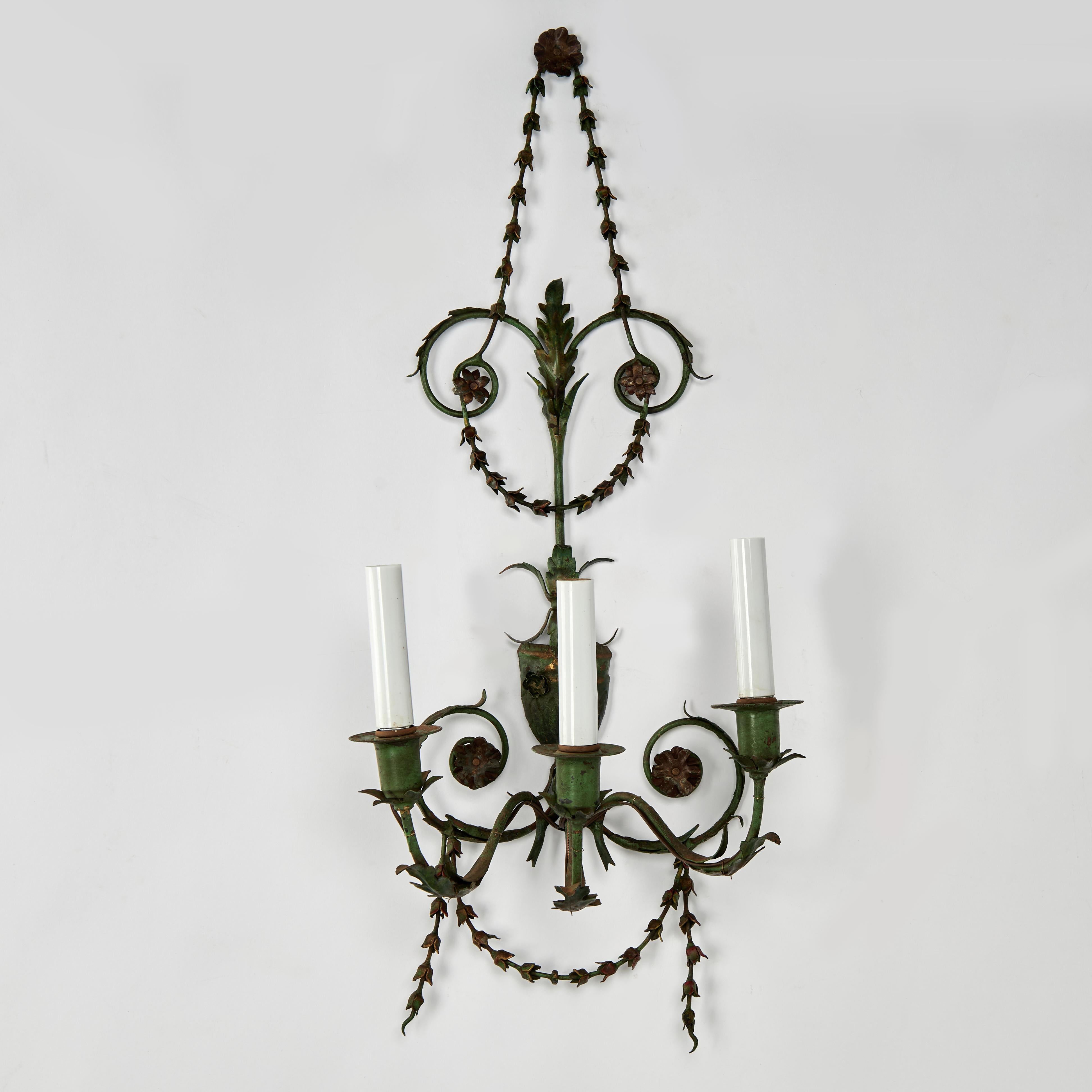 Standout pair of antique Italian three light wall sconces crafted in metal and brass in classical form with a contrived verdigris finish having floral wreaths, urns, medallions and acanthus leaves.