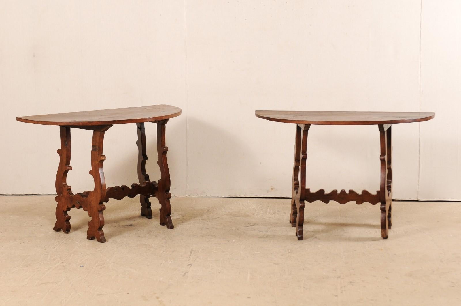 An Italian pair of walnut wood demilune consoles with lyre-legs from the 19th century. This pair of antique tables from Italy each feature half-moon shaped top which is raised upon a pair of sinuously carved and canted lyre-legs. The lyre legs are