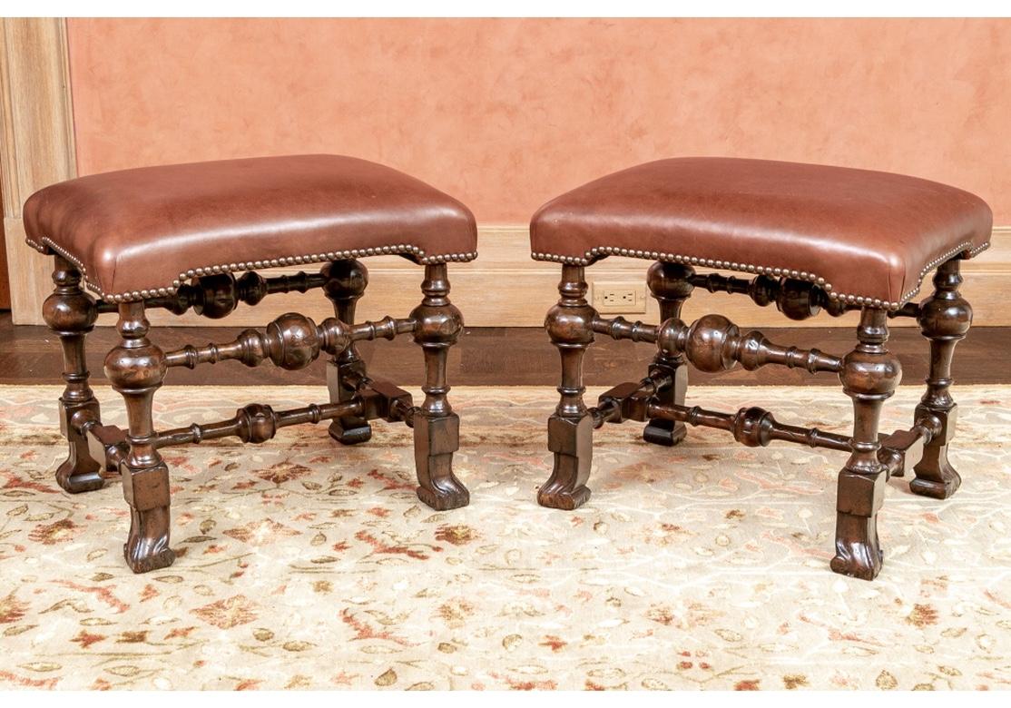 Stylish pair of Antique Foot Stools in Jacobean Style which have been refinished in a fine polished dark stain. The turned legs, upper and lower H stretchers with ball elements. The block legs with carved scrolled feet. The brown leather tops with