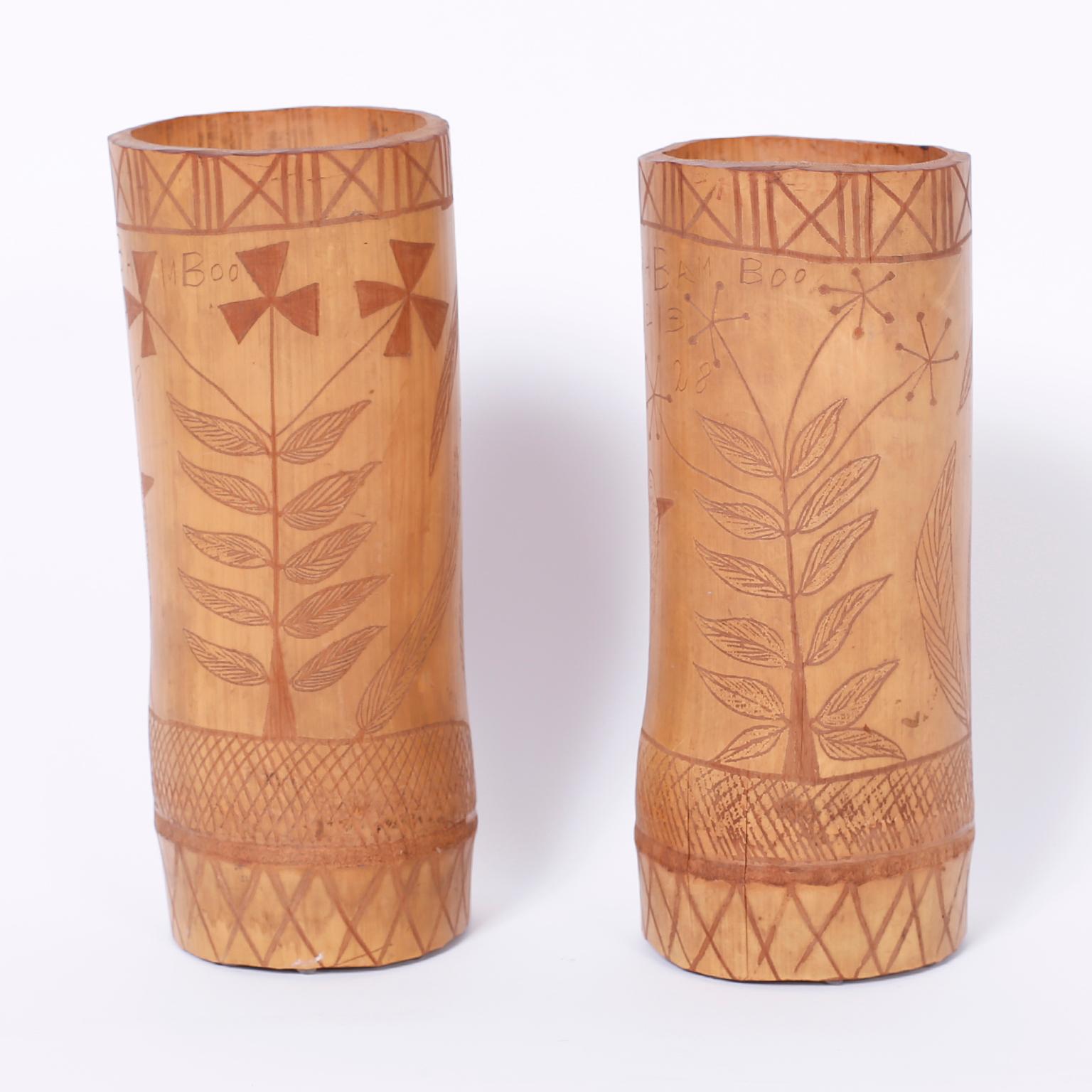 Folky pair of Jamaican vases or vessels crafted in bamboo with carved decorations of Palm Trees, birds, plants, and inscribed with the message Jamaican Bamboo Vase 1928. 

The height of the shorter vase is 10.5.