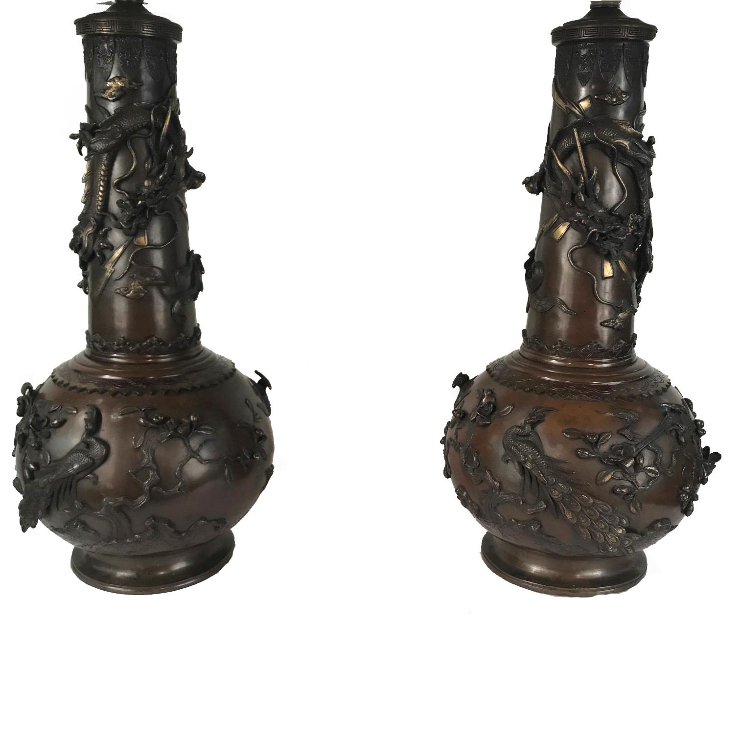 This handsome pair of lamps are at once highly ornamental and useful. An oversized pair of Japanese bronze vases of tall bottle form, each with a bulbous lower section embellished with birds amidst gnarled branches, leaves and buds raised in high