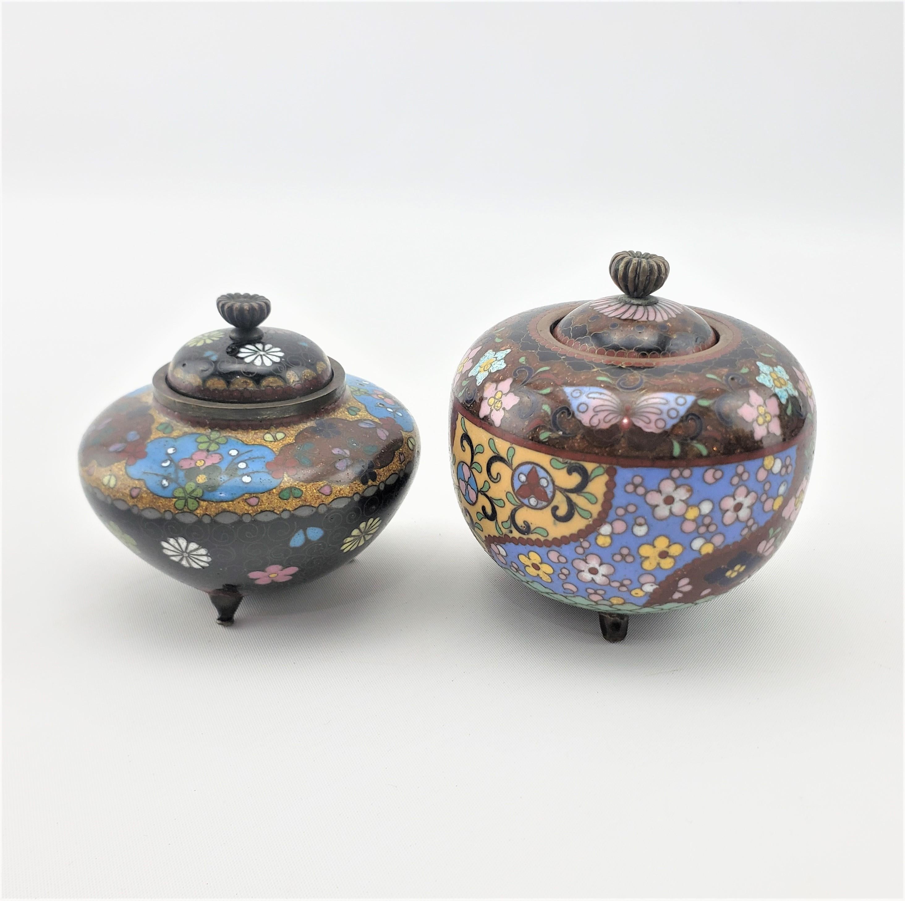 This pair of antique cloisonne covered jars or urns are unsigned, but originate from Japan from approximately 1900 in a Japanese export style. The pair is done in muted tones and are decorated with a floral motif.