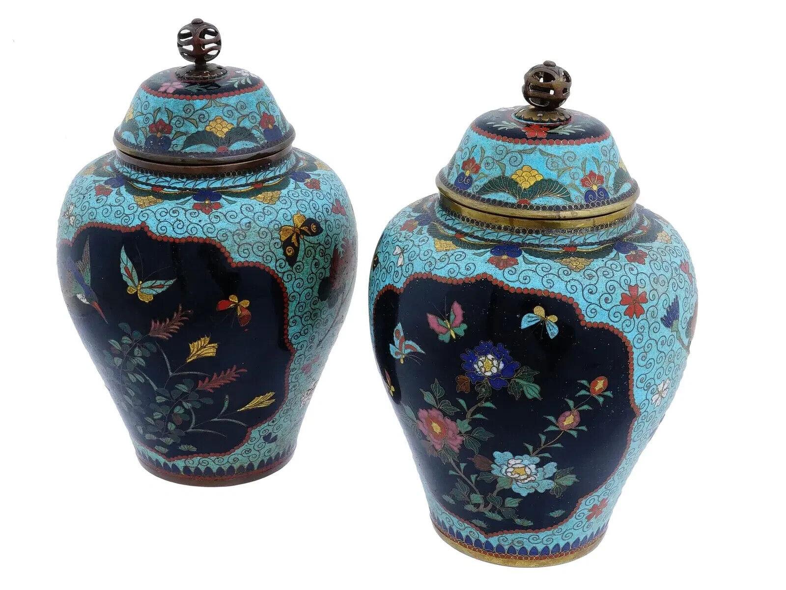 Pareja de jarrones antiguos japoneses con tapa de esmalte cloisonné de la era Meiji. Los jarrones tienen una forma similar: un cuerpo redondeado con una base ligeramente ahusada y una tapa abovedada. Cada tapa tiene un pomo calado de bronce en la