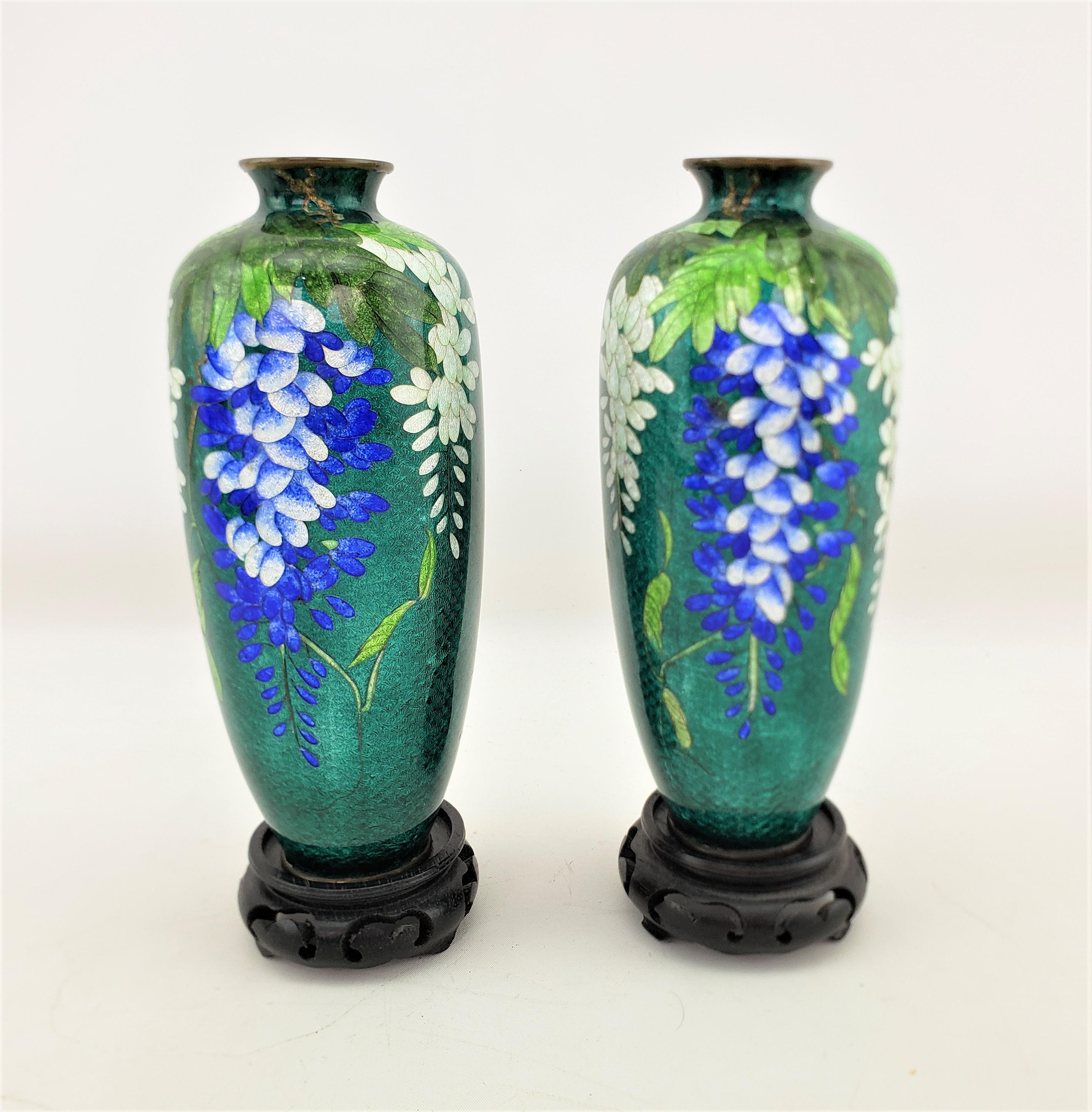 This pair of vases are unsigned, but presumed to have originated from Japan and date to approximately 1920 and done in an Anglo-Japanese style. The vases are done in engraved brass with a vibrant teal cloisonne enamel ground with bright blue and