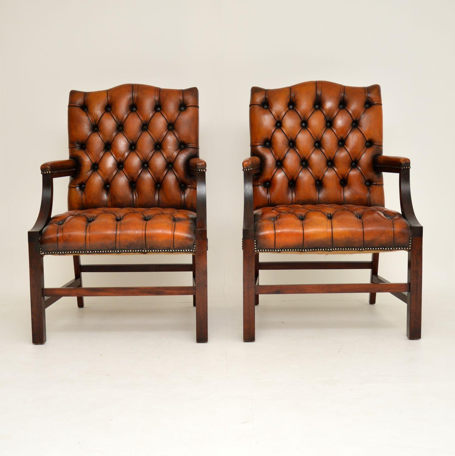 This pair of antique deep buttoned leather Gainsborough armchairs have fairly large, generous proportions and they have solid mahogany arms, legs and stretchers. They have hump backs, open arms with padded leather tops and cross stretchers between