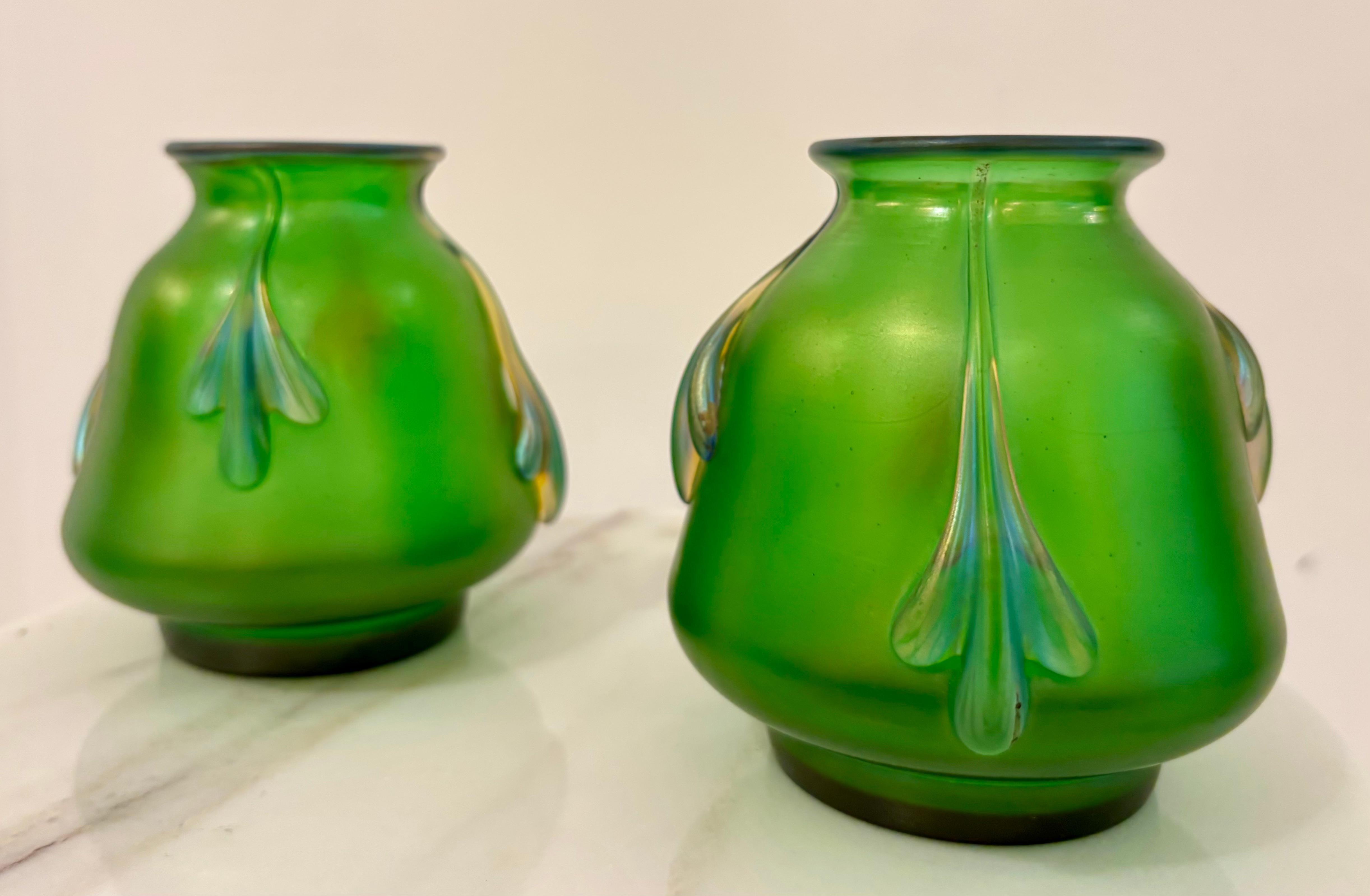 A rare and exquisite pair of antique Loetz iridescent glass vases, made in Bohemia around 1900 during the height of the Art Nouveau movement. Crafted in a lush emerald green glass, these petite vases feature applied pulled feather or leaf motifs in