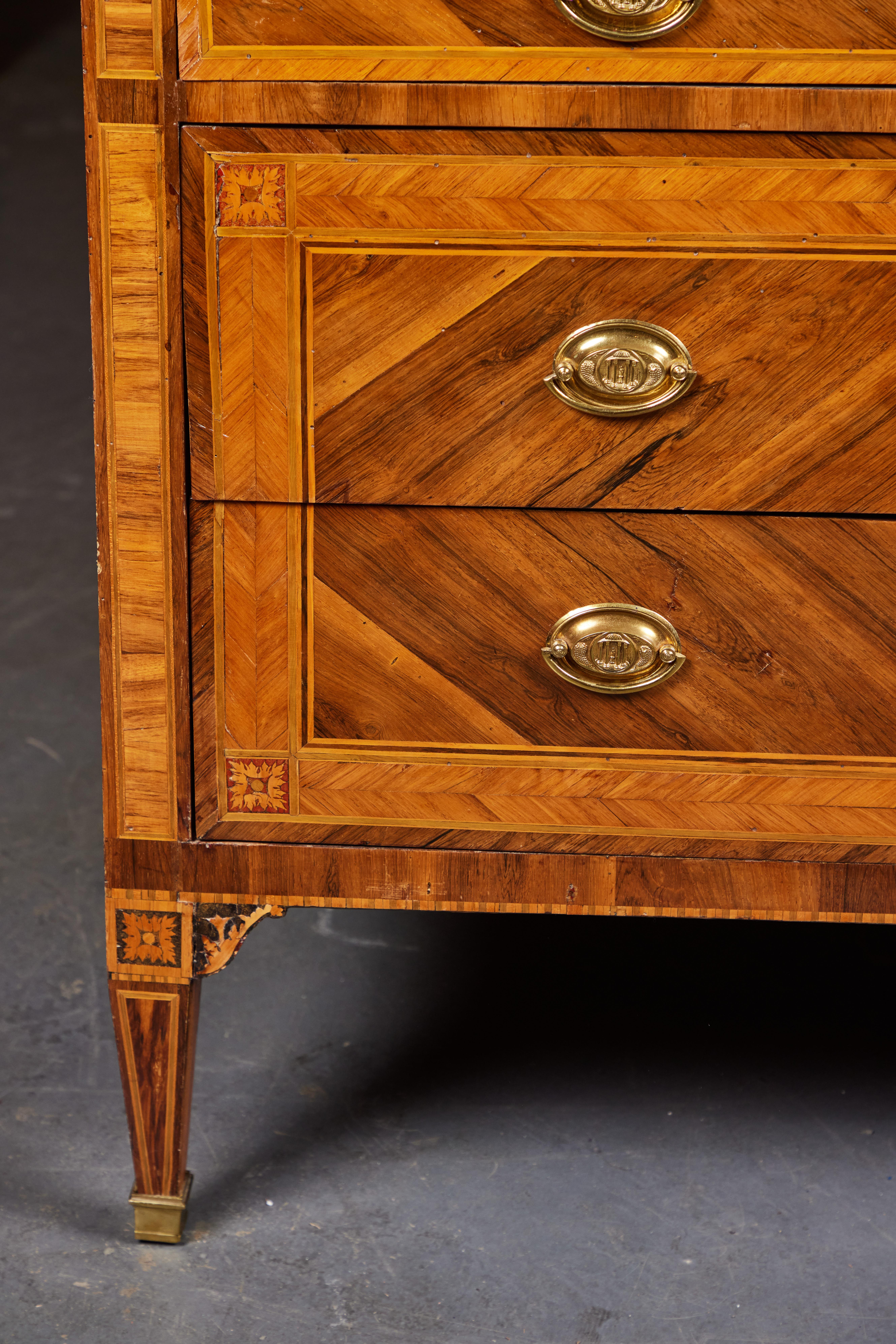 Beautifully finished, hand-carved, veneered and inlaid, two drawer, c. 1800 Northern Italian, Neoclassical commodes in book-matched walnut and fruitwood. The molded brass drawer pulls feature medallions with raised reliefs of columned, domed temples.