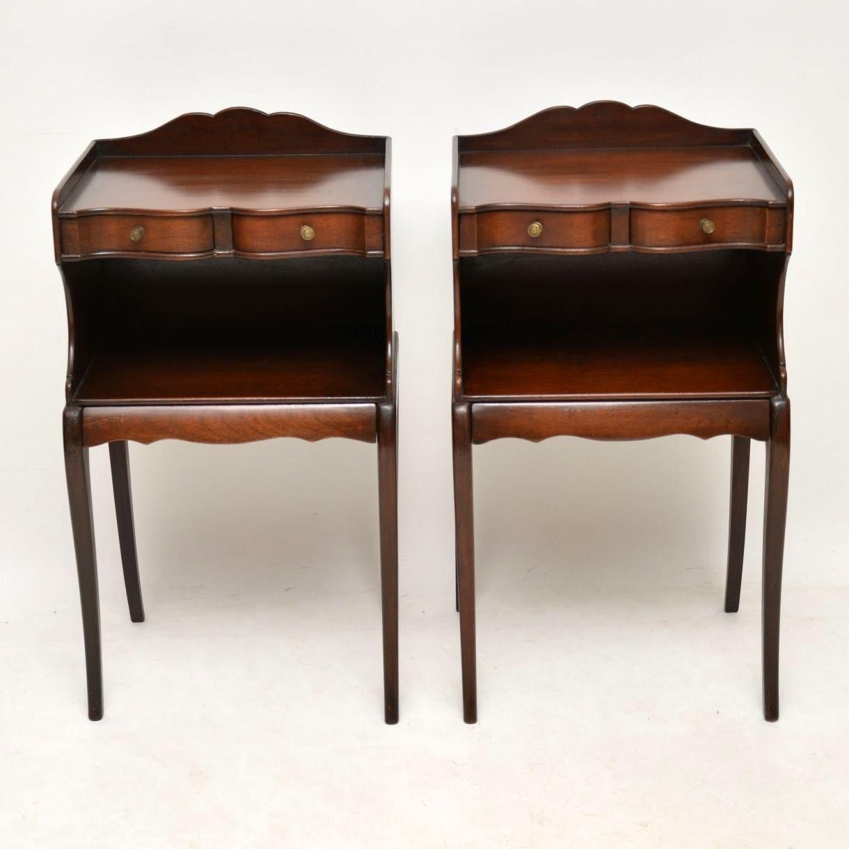 Pair of stylish antique mahogany bedside or lamp tables in the Regency style and dating from around the 1910-1920s period. They are very elegant with sabre legs on the backs and fronts. There are two shaped narrow drawers on the tops and another