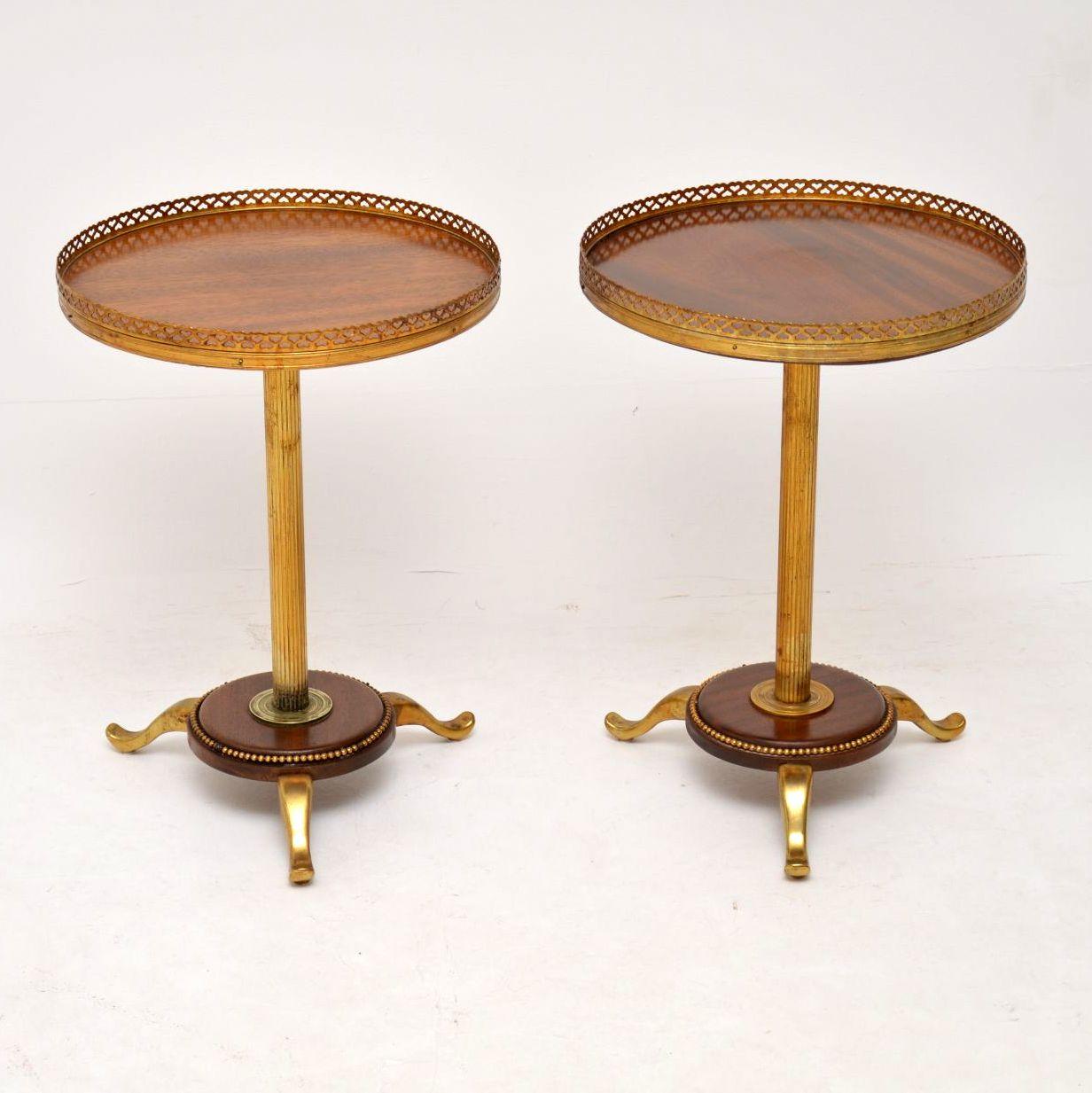 Unusual pair of antique wine tables with a combination of brass and mahogany. They have mahogany tops surrounded by brass galleries and brass fluted pedestals that sit on mahogany platforms with brass legs. They are in good original condition and I
