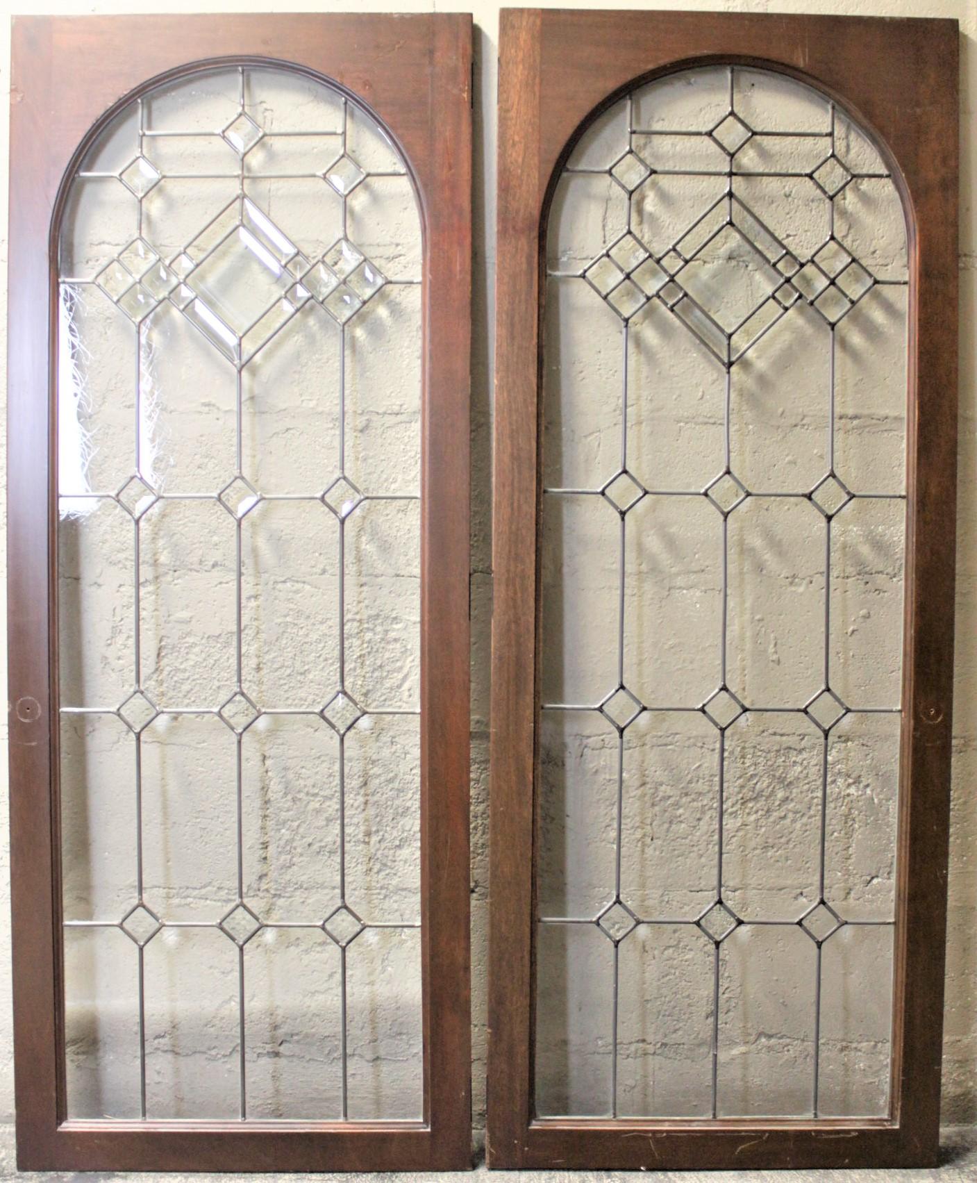This salvaged pair of cabinet doors are unmarked with respect to their maker, but presumed to have been made in the United States in circa 1935. The frames of the doors are mahogany with sound joinery on each corner. Each door features an arched