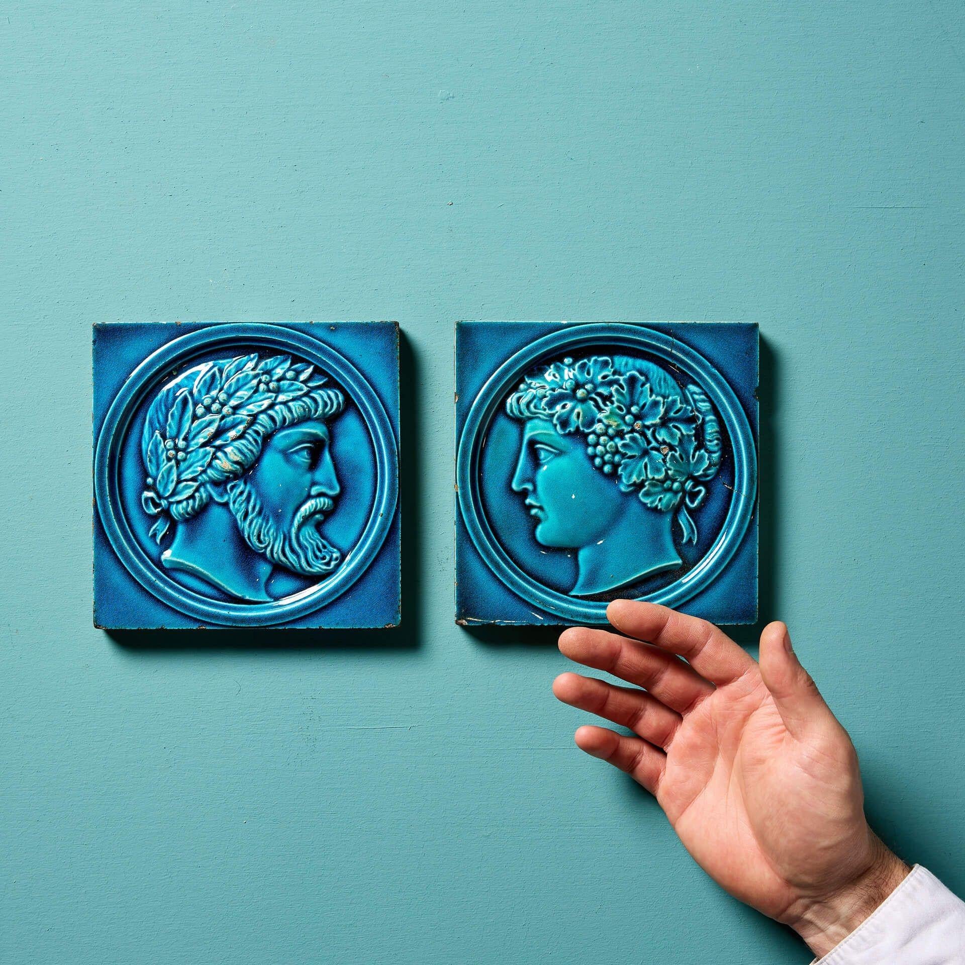 A pair of antique late 19th century Maw & Co tiles from Broseley Salop workshops in Shropshire.

In turquoise and dark navy blue majolica glaze, one 6-inch tile is decorated with the portraits of Greek noblemen wearing an olive wreath, together with