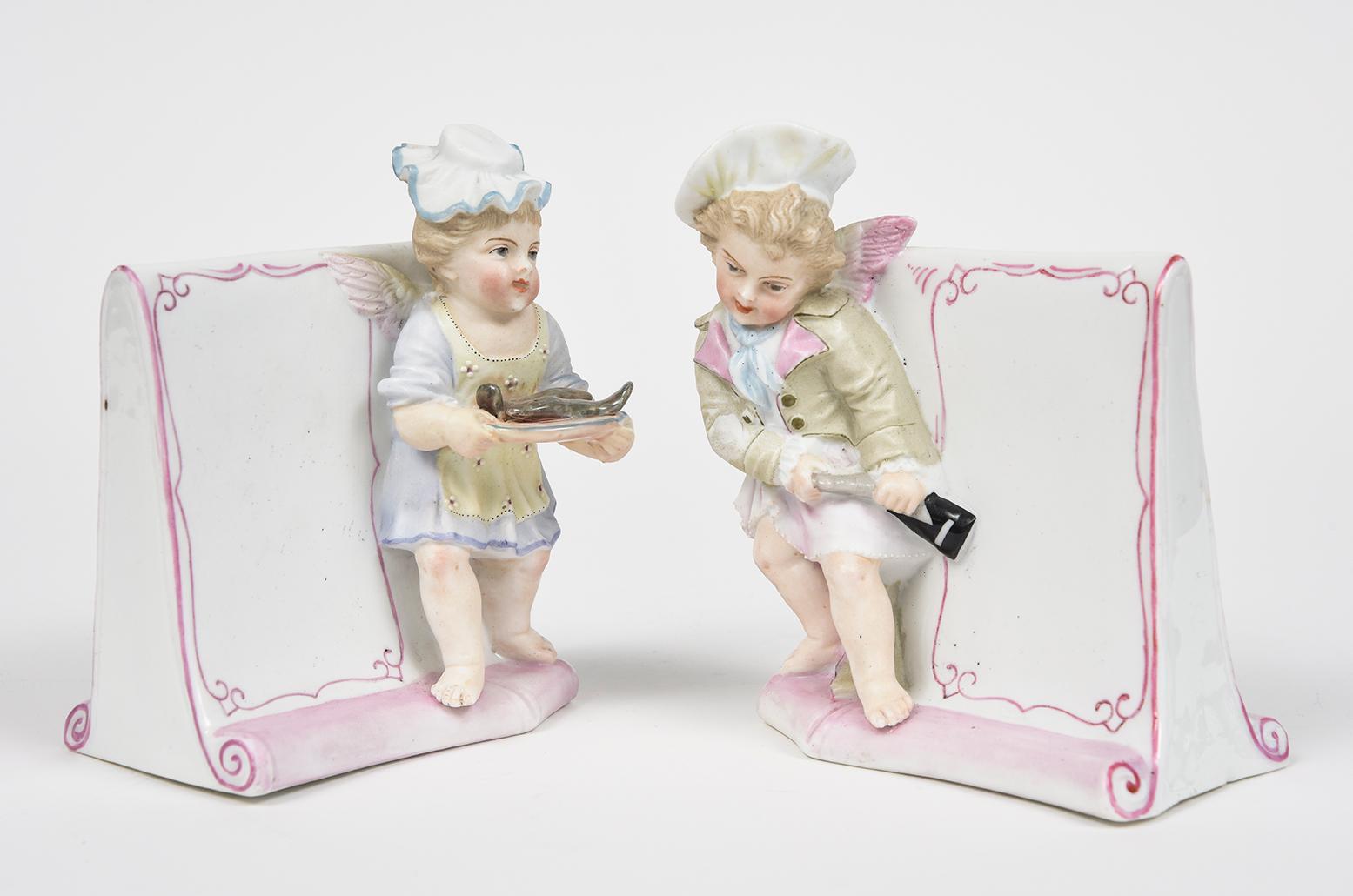 Pair of porcelain and bisque menus with barefoot serving cherubs. The male is opening a bottle of champagne and the female is serving fish on a platter. They are Meissen-like in style. Marked on the bottom 168T and a blue ink mark underneath that