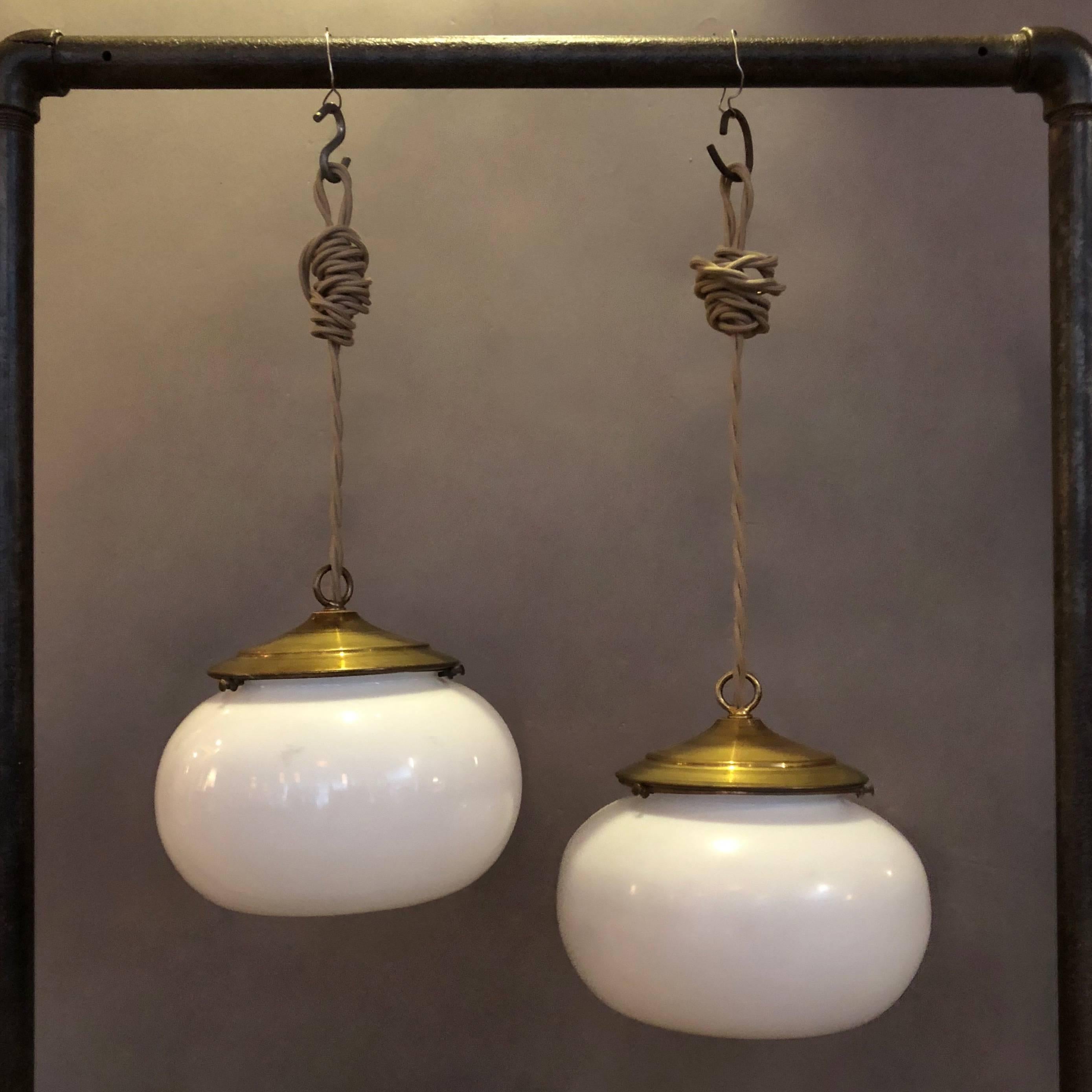 Pair of Industrial pendant lights feature antique, converted gaslight, orb shaped, open bottom, milk glass shades with wide brass fitters. The lamps are newly wired with 48 inches of braided cloth cord to accept 150 watt bulbs.