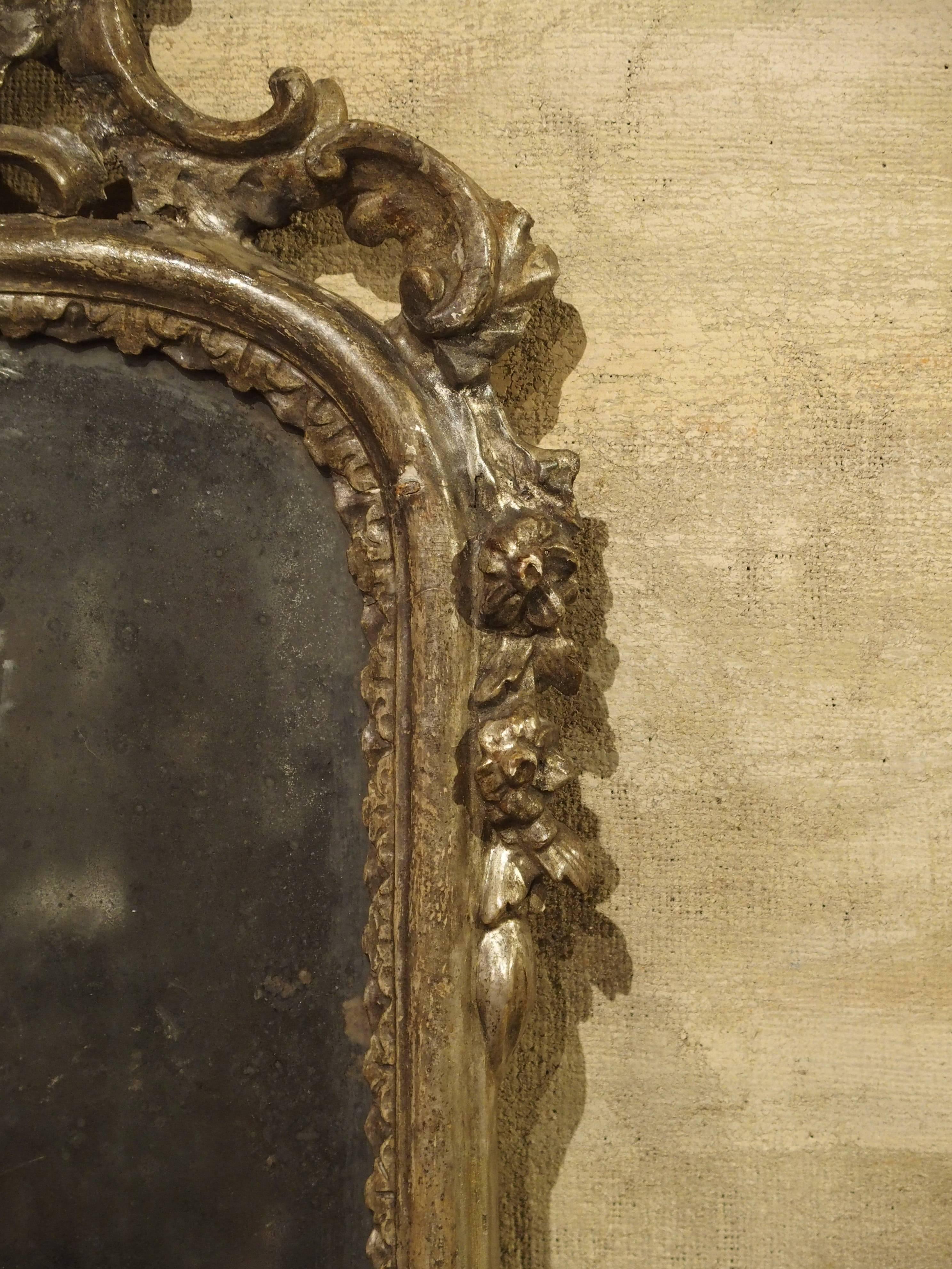 These rare mirrored wall sconces from Italy date to the mid-18th century. The silvered glass has the very desirable losses of silvering that would be seen on mirrors of this age today. The wooden frames have old silver leafing with the acanthus