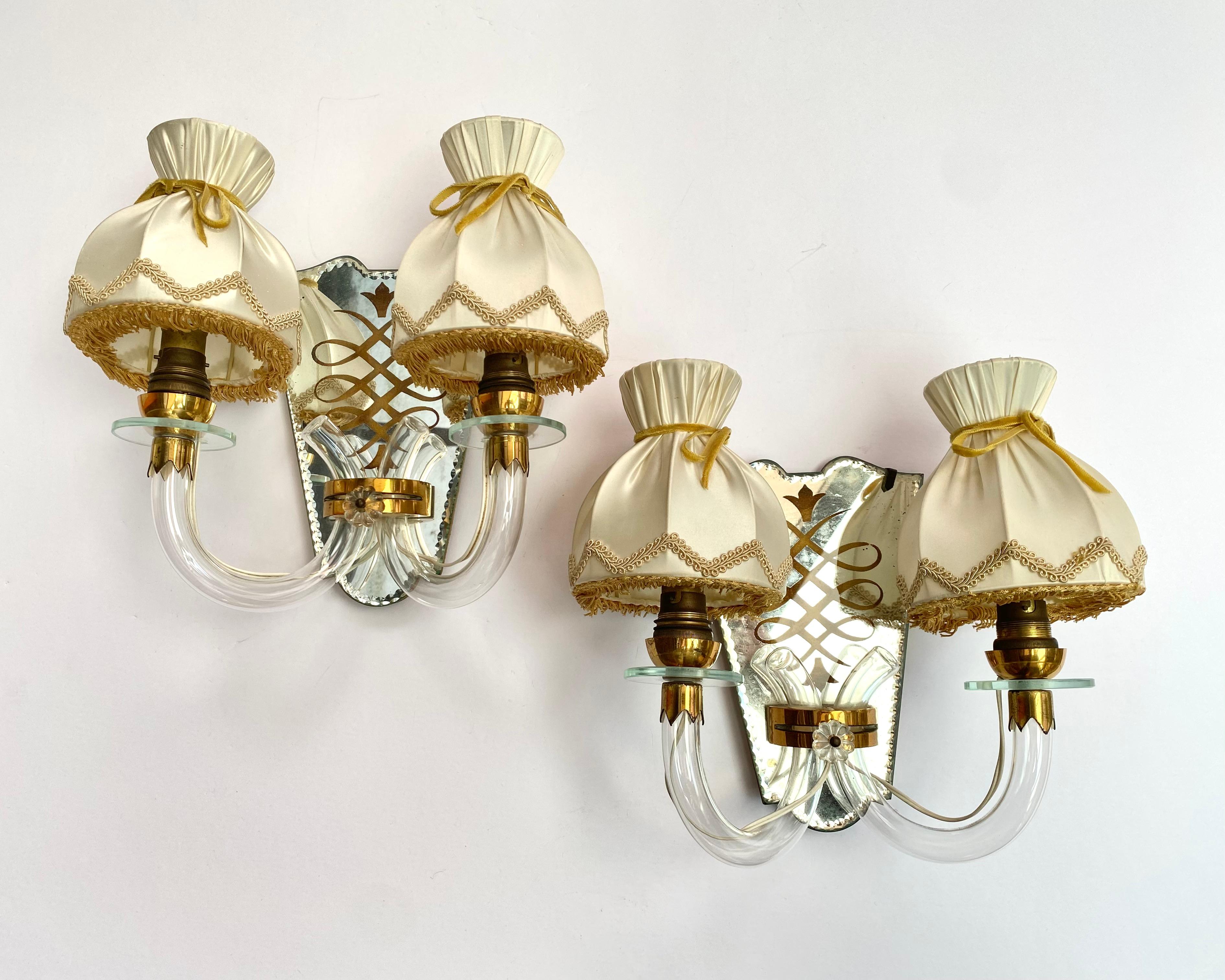 Pair of two-arm brass Italian 1920s mirrored and etched wall sconces with textile shades (1970s).

Nice hand crafted detailing including cut scalloped mirrored edges. Each sconce uses two candelabra base bulbs.

Convert your space into a 1920s