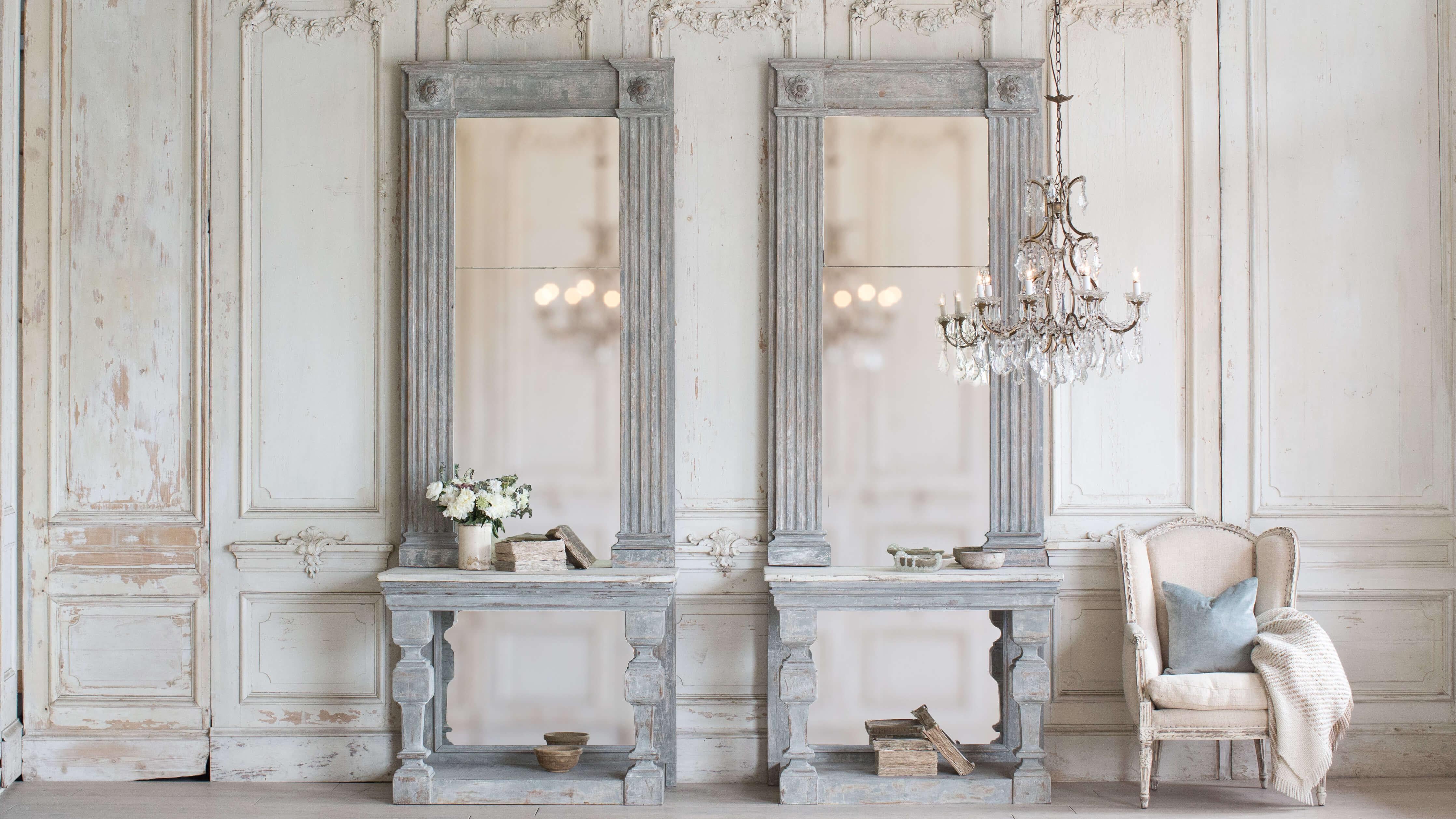 Absolutely breathtaking pair of antique French consoles with aged, antique mirror. A timeless carved column and rosette motif adorns the outer frame. The pair of consoles are finished in a worn, deep French grey with aged white table tops. Elegant