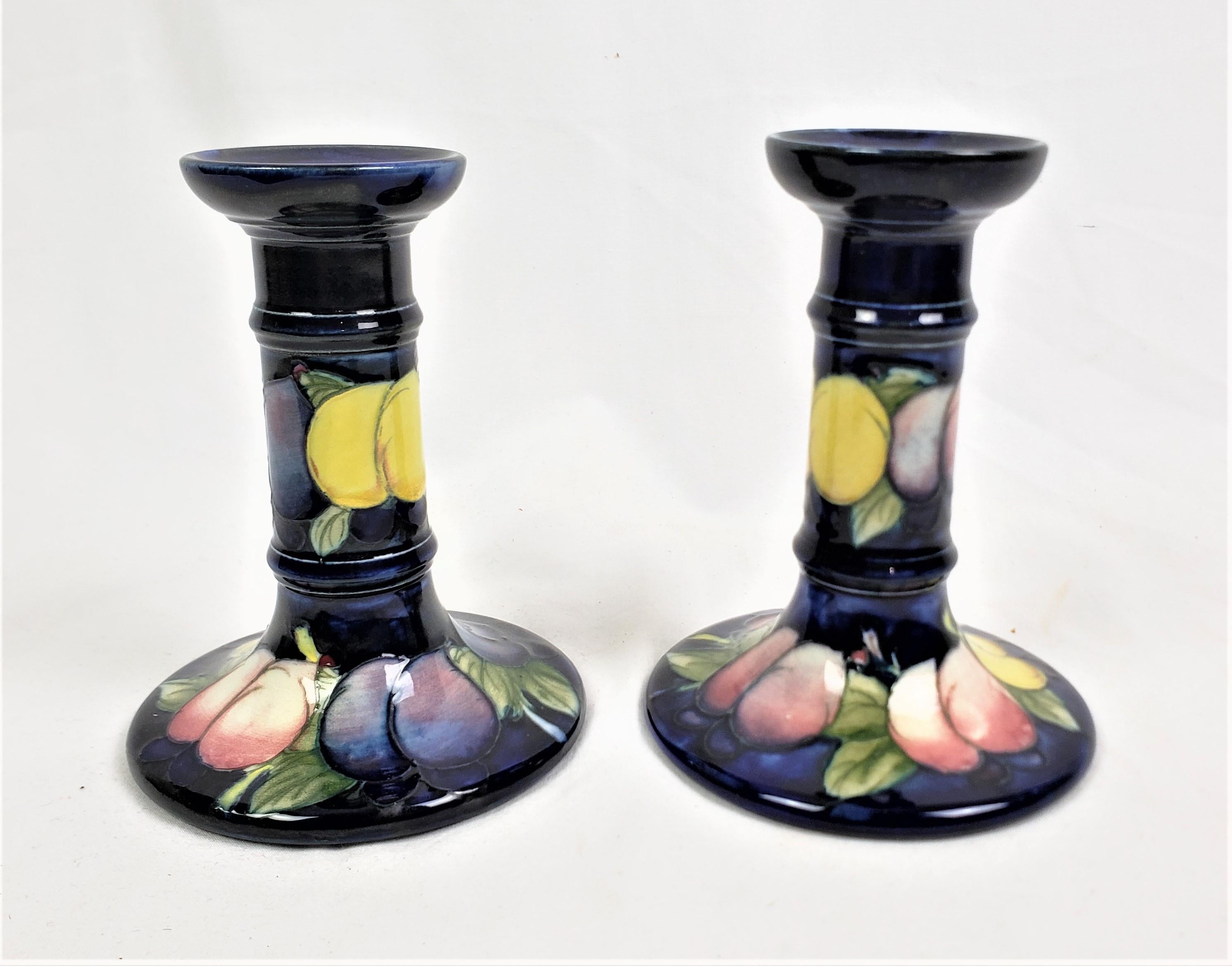 This pair of art pottery candlesticks were made by the well known Moorcroft Pottery factory of England and date to approximately 1920 and done in their signature style. The candlesticks are done with Moorcroft's cobalt blue ground, with the Wisteria