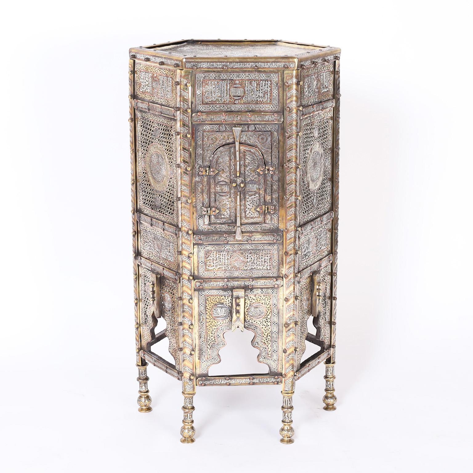 Pair of 19th century Moroccan stands crafted in brass and copper with silvered highlights over an elaborate hexagon form, composed with geometric designs, perforated panels with center medallions, moorish cabinet doors and arches on turned legs.