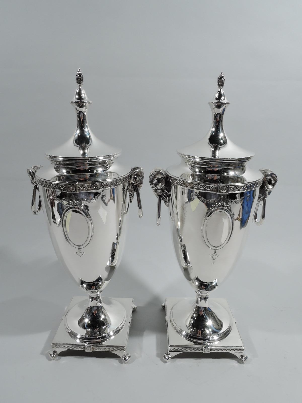 Pair of Pompeiian sterling silver covered urns. Made by Mt Vernon in Mount Vernon, New York, ca 1920. Each: Tapering urn on raised round foot mounted to square base on splayed volute supports. Cover double-domed with vasiform finial. Side-mounted