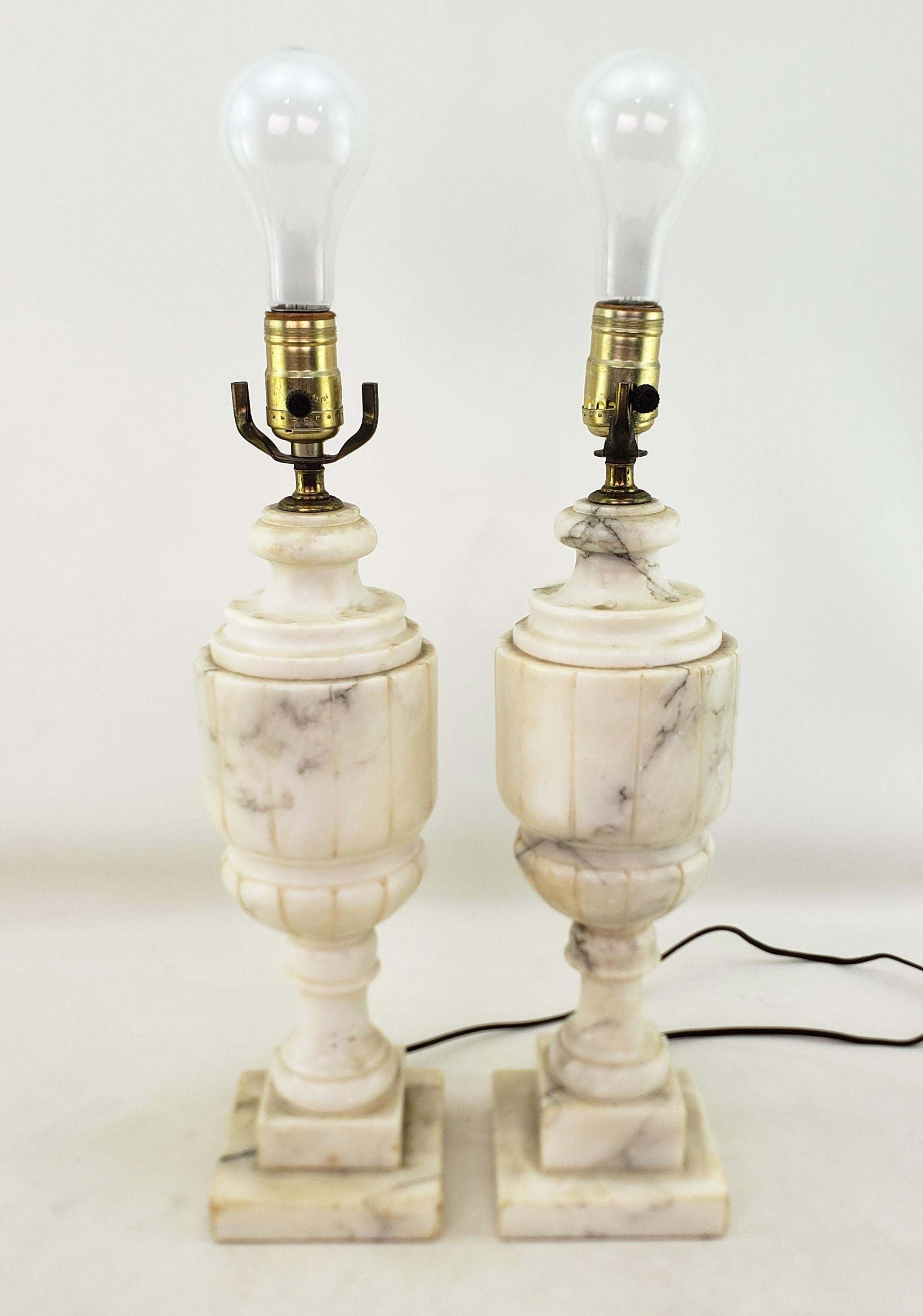 This pair of antique lamp bases are unsigned, but presumed to have originated from Italy and date to approximately 1920 and done in a Neoclassical Revival style. The lamps are composed of veined alabaster with a ribbed urn form and alabaster block