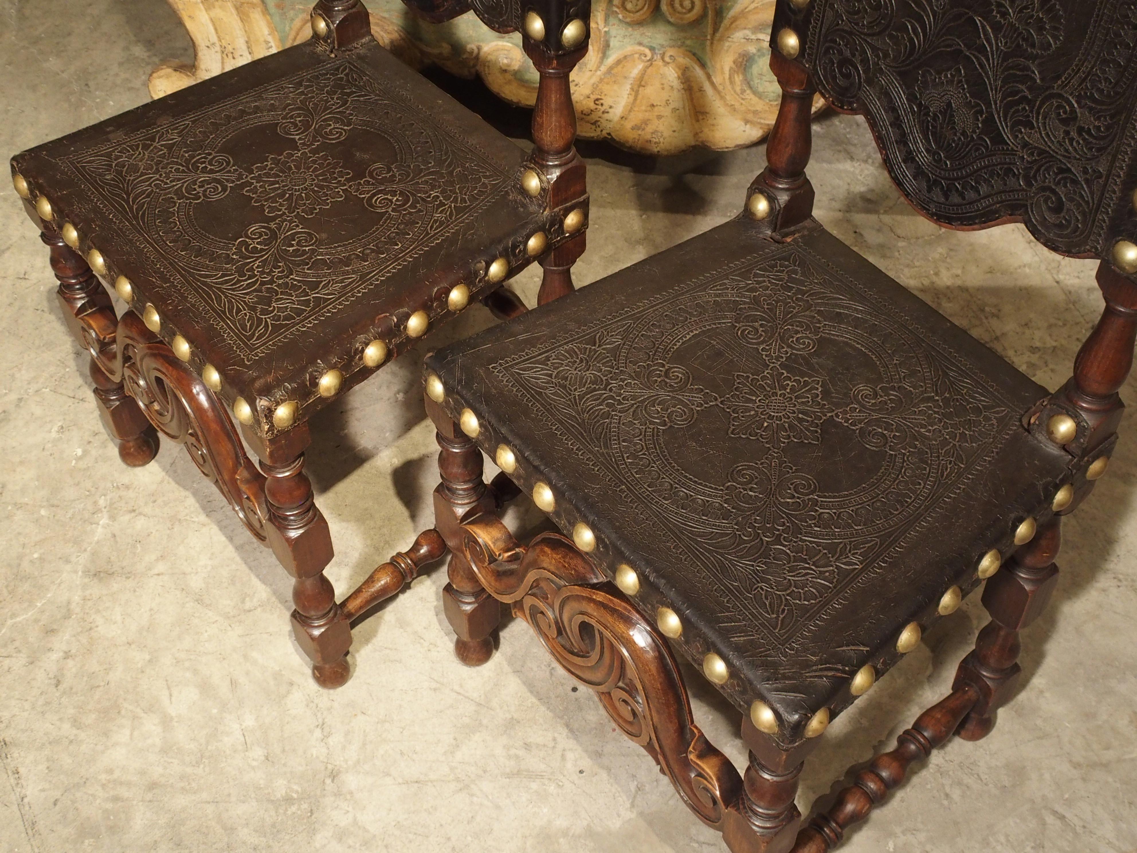 These rich antique Portuguese chairs have highly detailed leather backs and seats. The leather is attached to the carved wood frames by large brass nailheads, and the motifs on the leather include flowers, leaves, scrolls, and large central