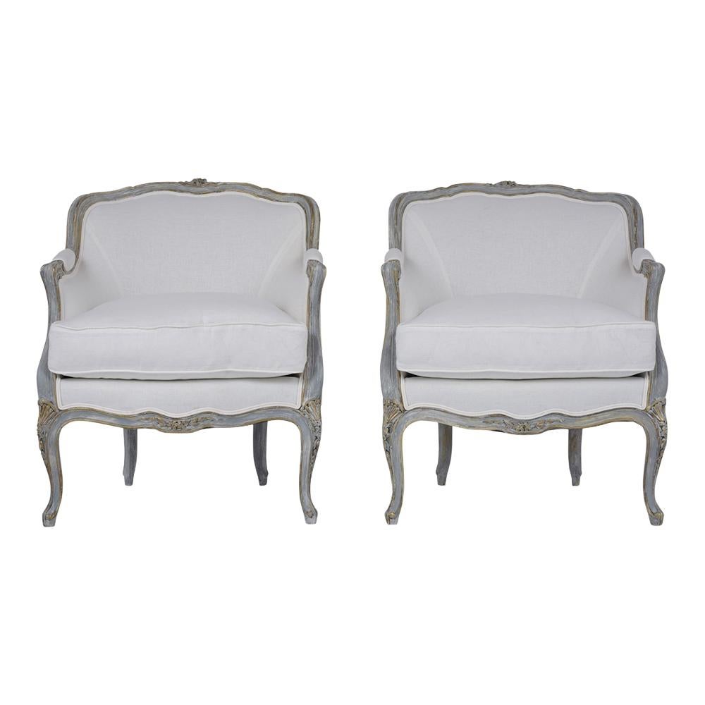 This Pair of French Antique Louis XV Bergeres have been professionally restored, made out of walnut wood, and is newly painted in a grey color with gilt accents and distressed finish. These armchairs feature a curved back design with hand-carved