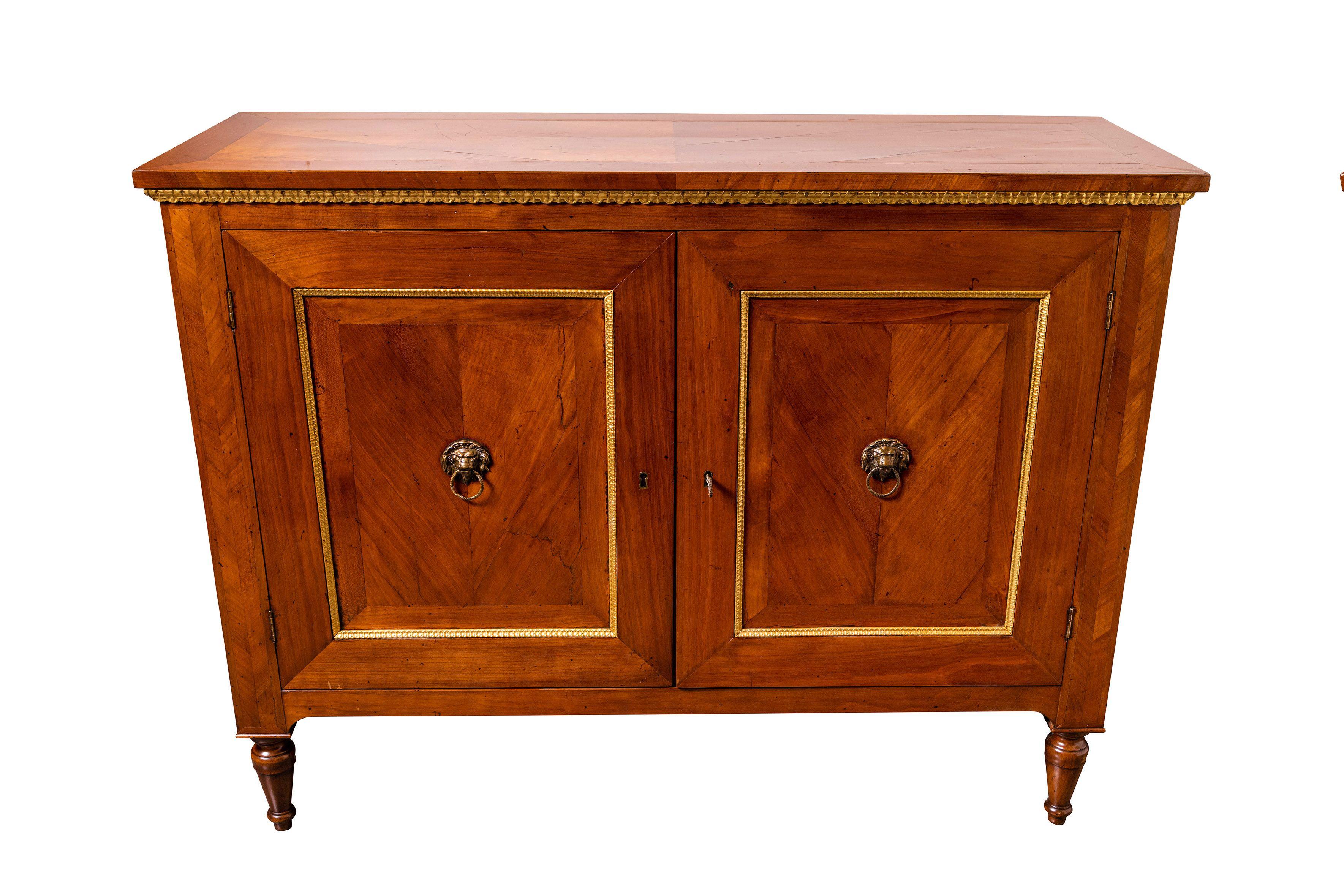 An impressive, sleek, mated pair of c. 1885, hand-carved, paneled, two door cabinets from the Emilia Romagna region of Northern Italy. Each veneered in book matched walnut. Both edged in gilded trim and finished with original, gilt bronze lion's