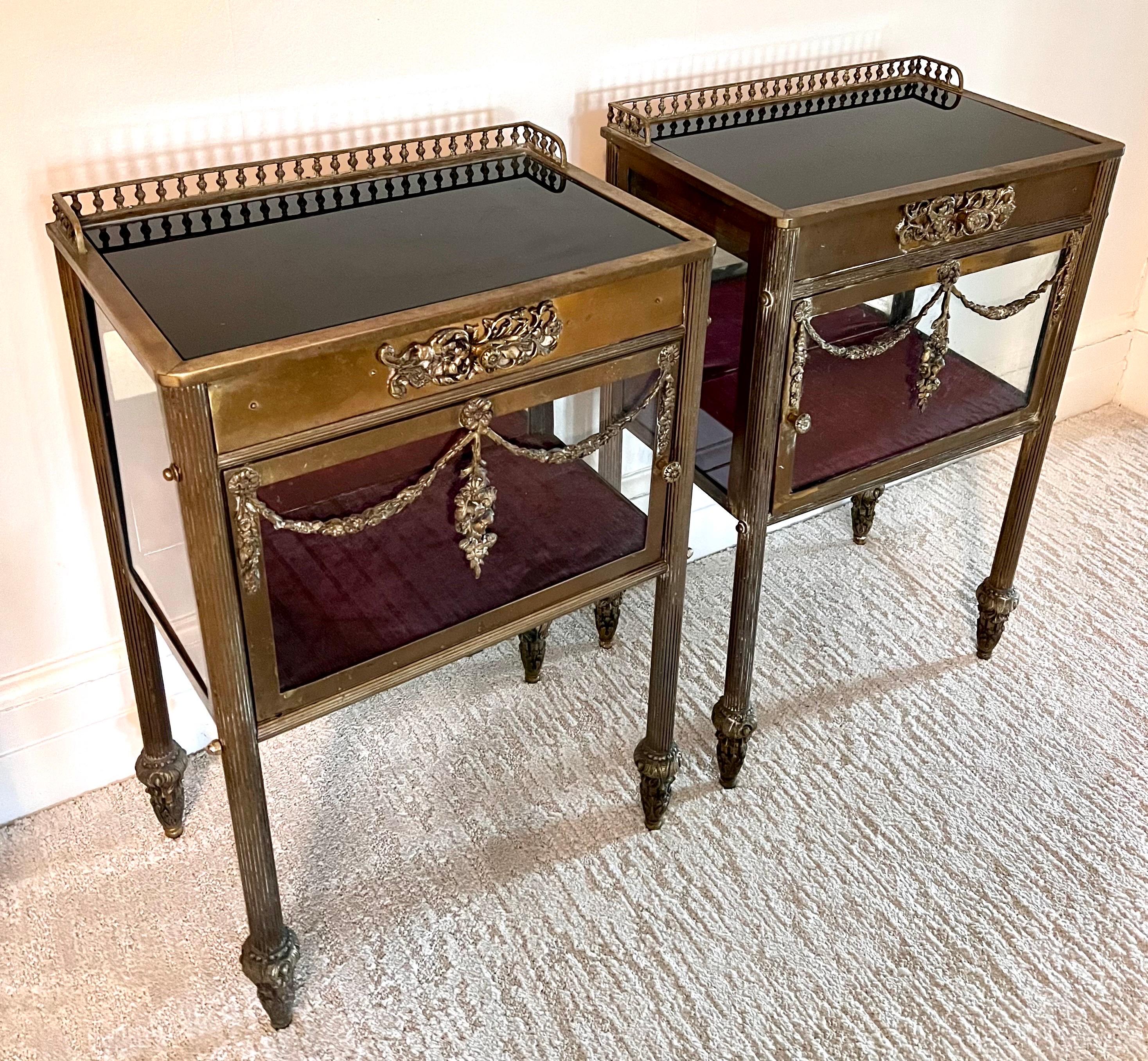 Antique 19th century French patinated brass and glass cased vitrine nightstands raised on fluted legs. Top is black glass with gallery and one drawer. Glass on front door and sides.
Mirrored glass inside back. Beautiful ornamental mounts decorate