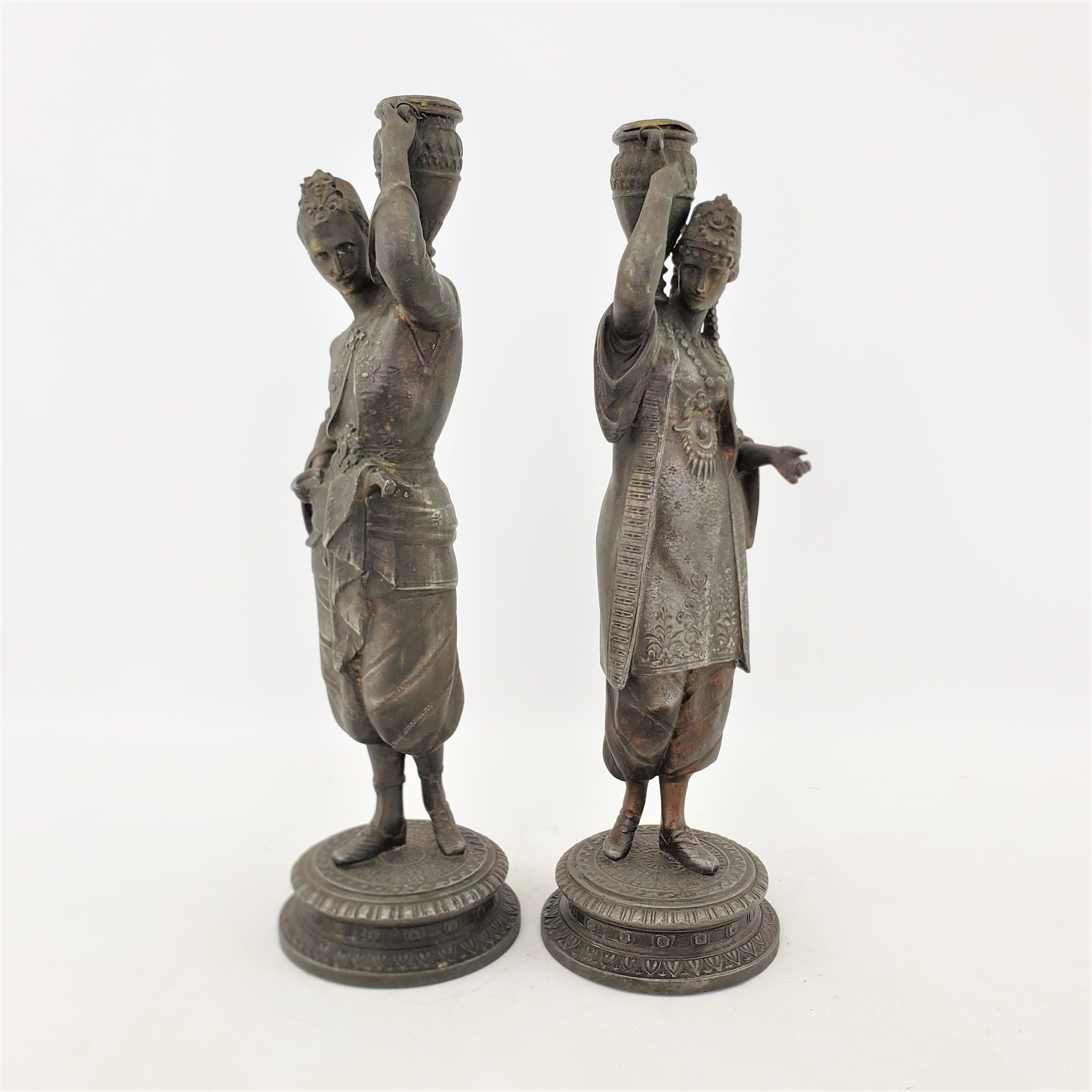 This pair of antique candlesticks are unsigned, but presumed to have originated from Austria and date to approximately 1900 and done in a Neoclassical Revival style. These sculptural candlesticks are composed of spelter with a patinated finish and