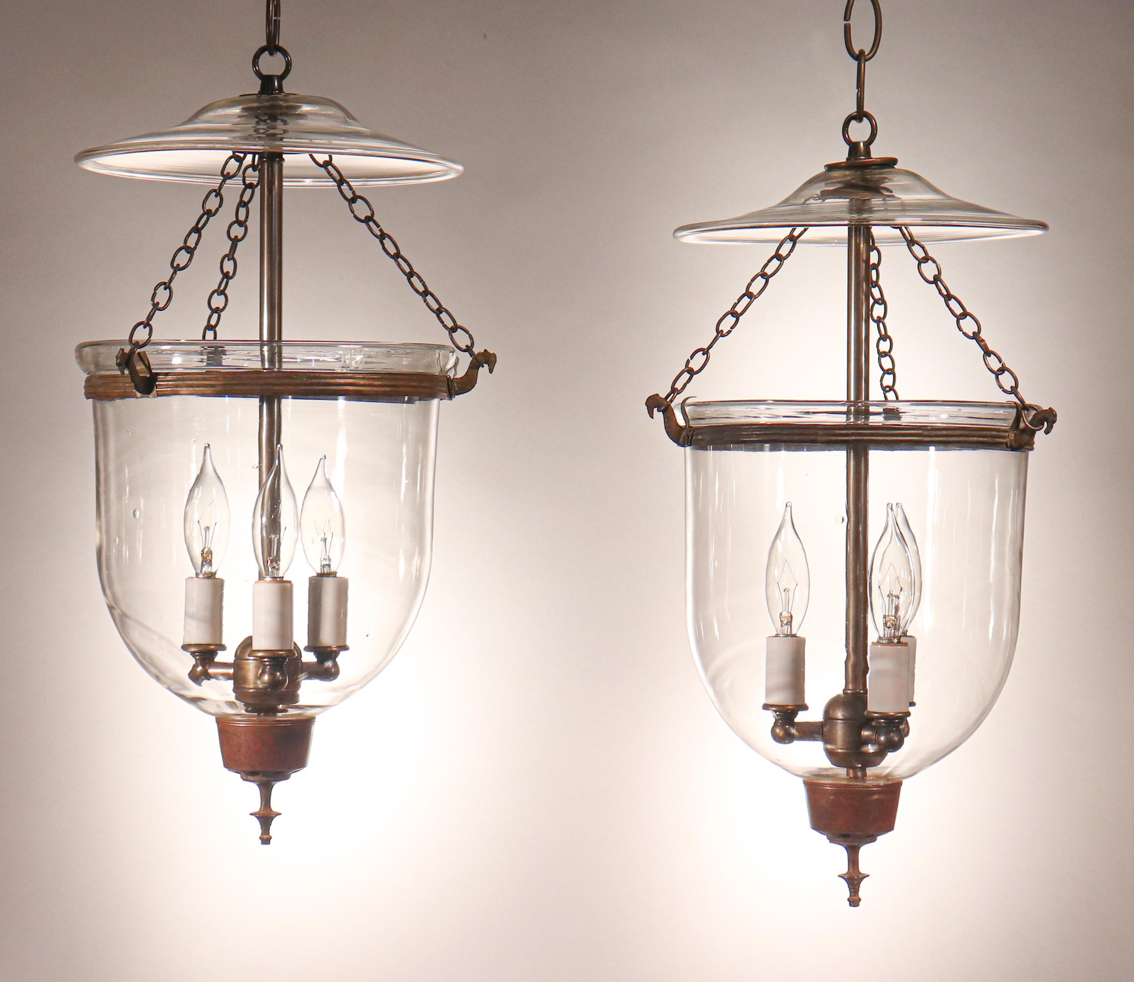 A rare, well-matched pair of petite English bell jar lanterns, circa 1870. These antique pendants feature excellent quality hand blown glass and original rolled brass bands and finials/candleholder bases. The fixtures have been newly electrified,