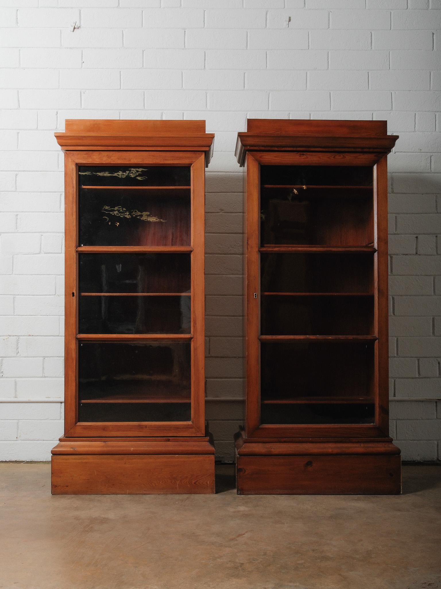 Cette paire de bibliothèques anciennes en pin offre un charme classique du 19e siècle avec ses tons chauds, ses lignes simples et ses rangements fonctionnels. Chaque meuble présente une silhouette haute et élégante avec une couronne étagée, une