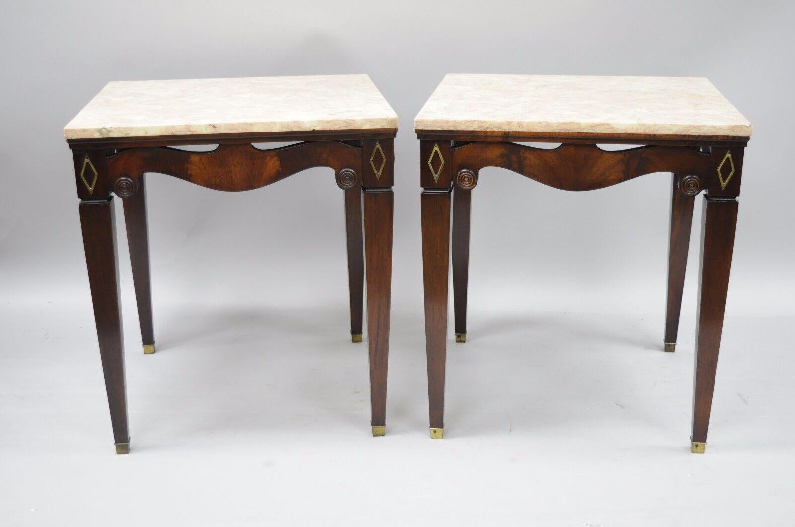 Pair of antique pink marble-top mahogany end tables in the Regency style. Possibly by Weiman. Unmarked. Item features pink square marble tops, flame mahogany veneer, pierce carved skirt, wood construction, beautiful wood-grain, brass accents, felt