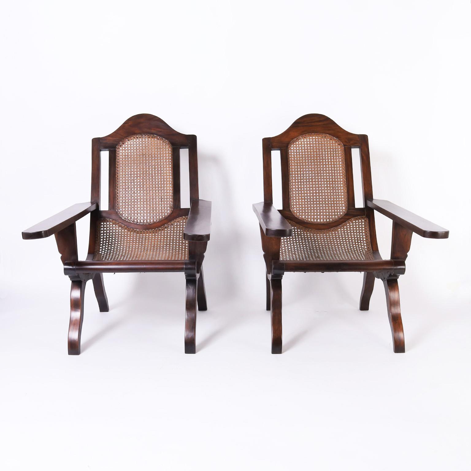 Standout pair of antique British colonial planters chairs crafted with mahogany in an unusual elegant form having inclined caned seats, caned backs, and leg rests.