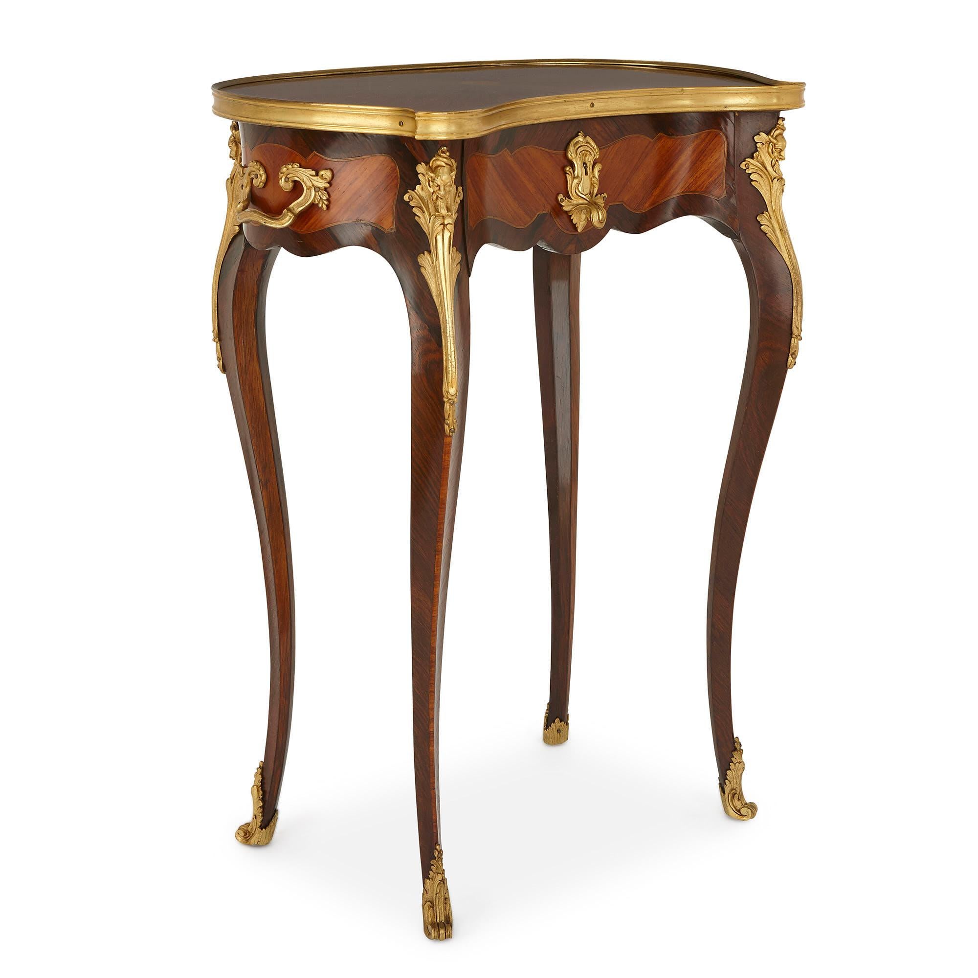 Each occasional table features four scrolled gilt bronze feet, which extend upwards to form rosewood cabriole legs. These are decorated, on their tops, with Rococo style gilt bronze mounts, cast as grotesque masks. On each, the legs support the body