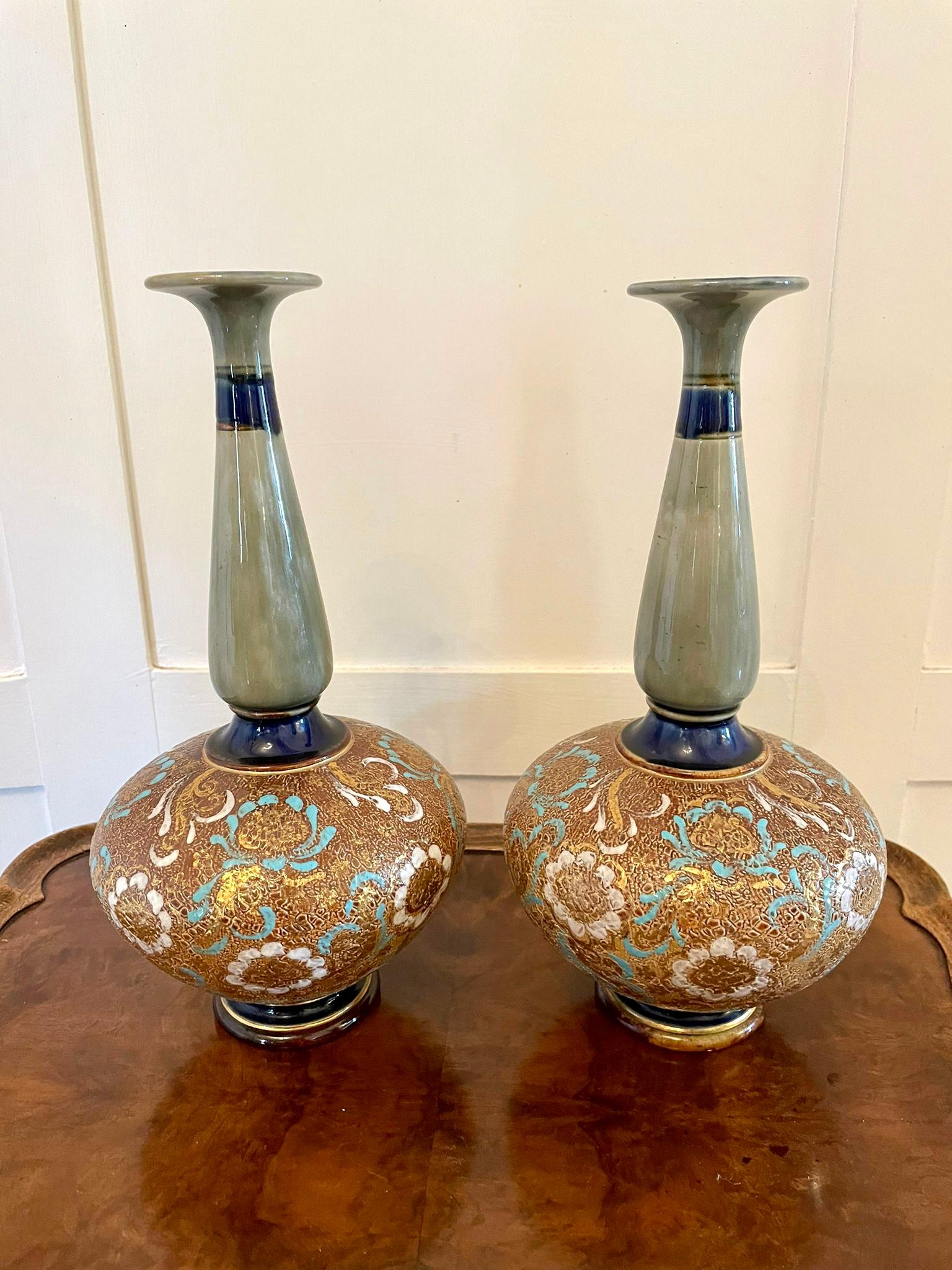 Paar antike Vasen von Royal Doulton mit schlankem Hals und rundem Fuß. Die Körper sind mit Blütenblättern aus weißem Gold und blauem Email über dem strukturierten Grund versehen, die Hälse und Füße in Oliv, Grün, Gold, Braun und Blau. Sie sind mit