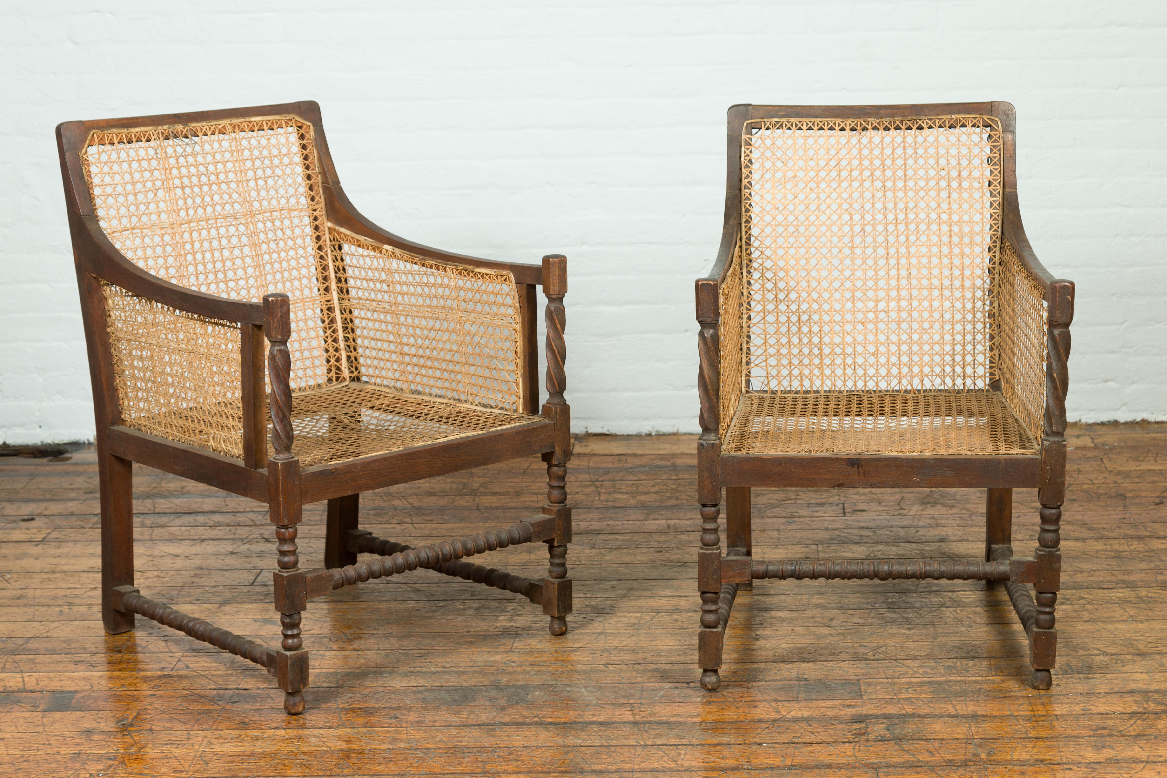 A pair of antique Thai armchairs from the 19th century, with rattan seats and backs. Created in Thailand during the 19th century, this pair of armchairs charms us with its rustic presence. Showcasing rattan backs and seats, the chairs are adorned