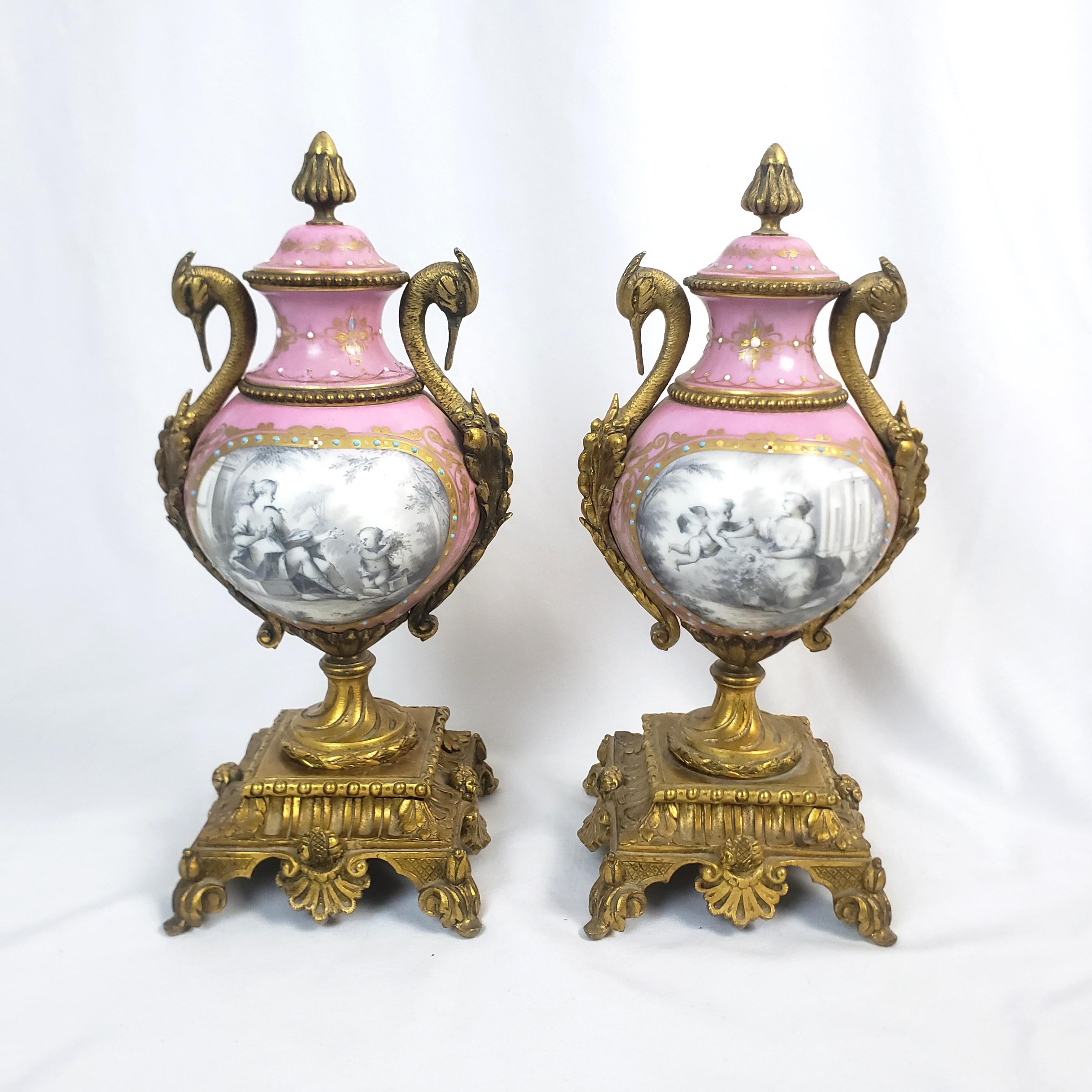 This pair of antique garnitures are unsigne, but presumed to have originated from France and date to approximately 1875 and done in the Sevres style. The garnitures are done in porcelain with ornate gilt bronze finial, stylized figural swan handles