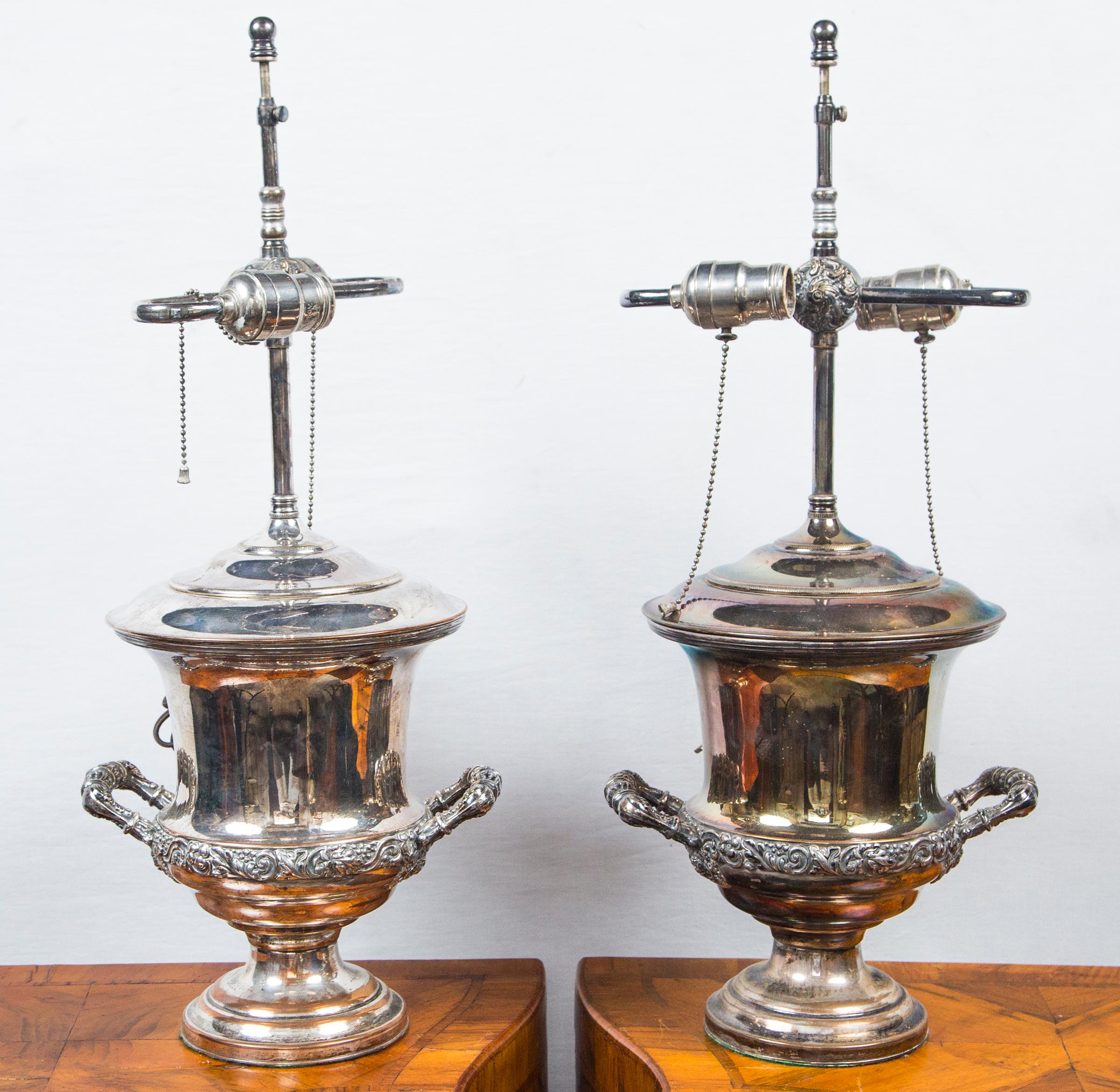 Each has been converted to table lamps, with a wire coming through the lid of the urn. Bleeding of silver, exposing the copper underneath. Unmarked. Decorative bands of grapes, grape leaves and vines. 
The width from handle to handle is 9 inches.