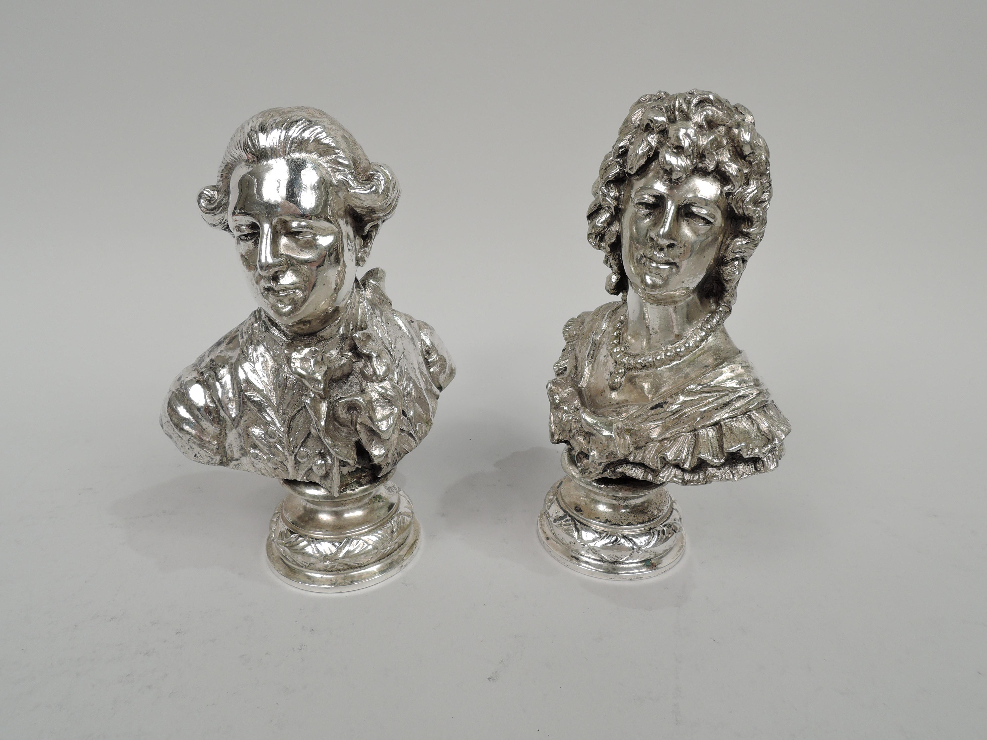 Pair of turn-of-the-century cast silver busts of ancien regime courtiers. The woman evokes a Baroque beauty from the reign of Louis XIV with an imperious face softened with ringlets, a necklace of walnut-sized pearls around a bare throat, and a