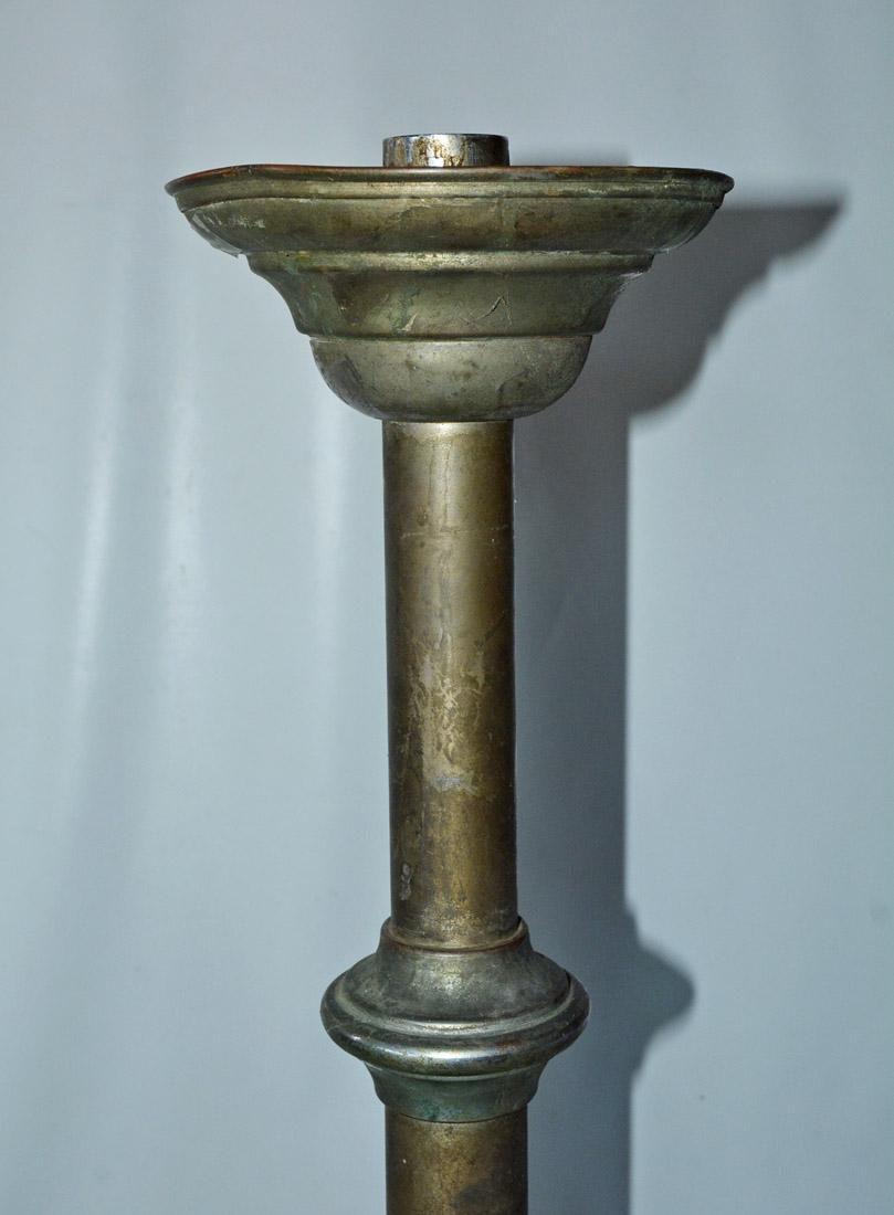 The pair of tall antique altar candlesticks or torchieres are made of silver-over-copper. Starting at the top with a candle socket and attached bobeche, the design is divided into four equal parts attached to a round base which is weighted