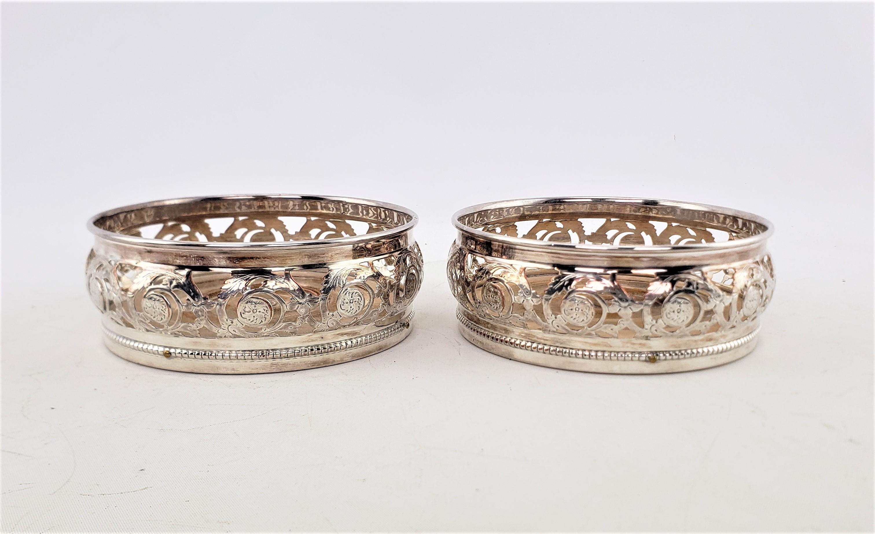 This pair of matching silver plated bottle coasters are unsigned, but presumed to have originated from England and dating to approximately 1920 and done in the Victorian style. These bottle coasters have pierced galleries with a floral motif and