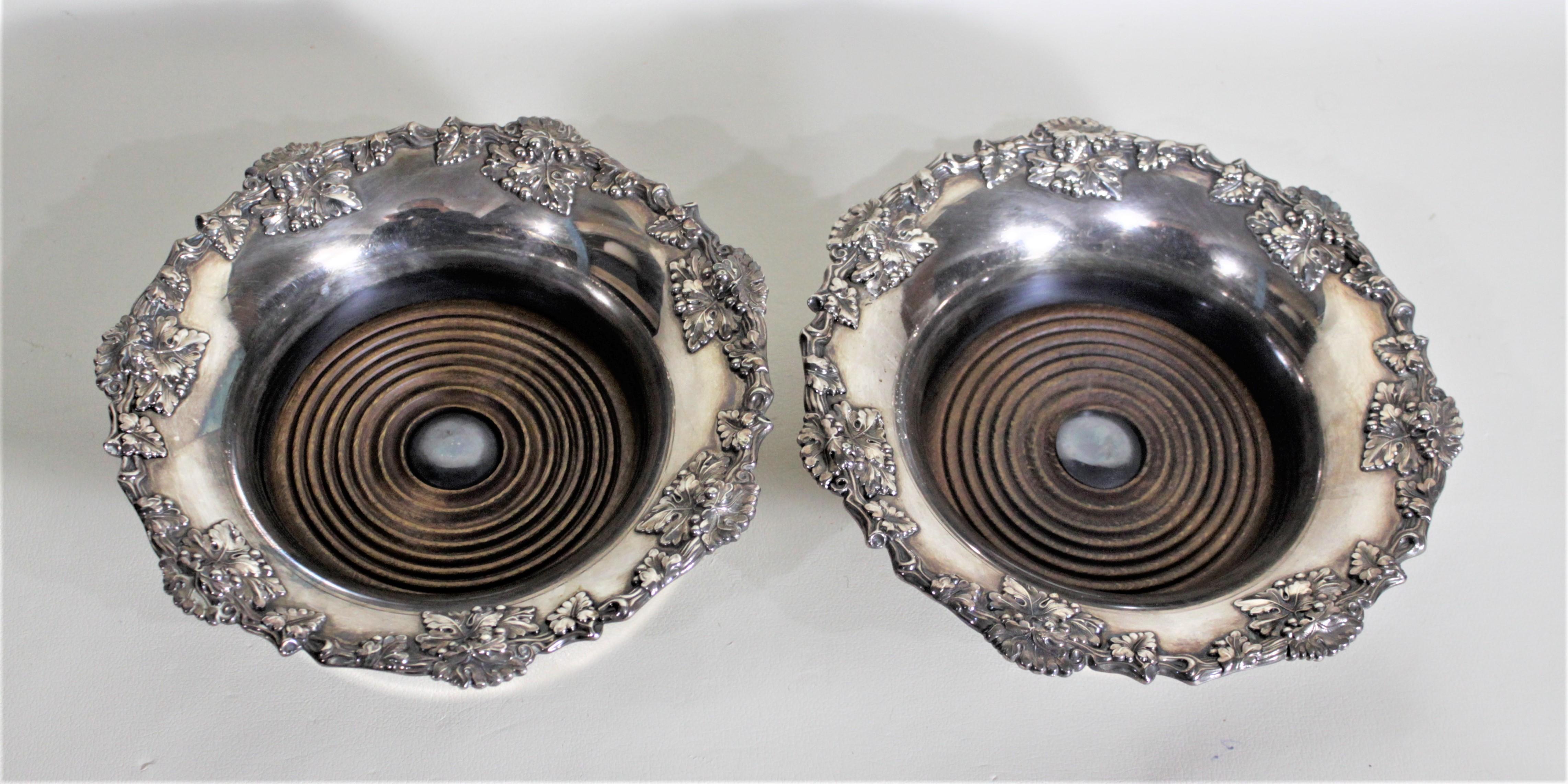 This pair of silver plated antique bottle coasters are completely unmarked, but presumed to have been made in England in circa 1910 in the period Edwardian style. The rims of these coasters are ornately decorated with a leaf and berry motif and the