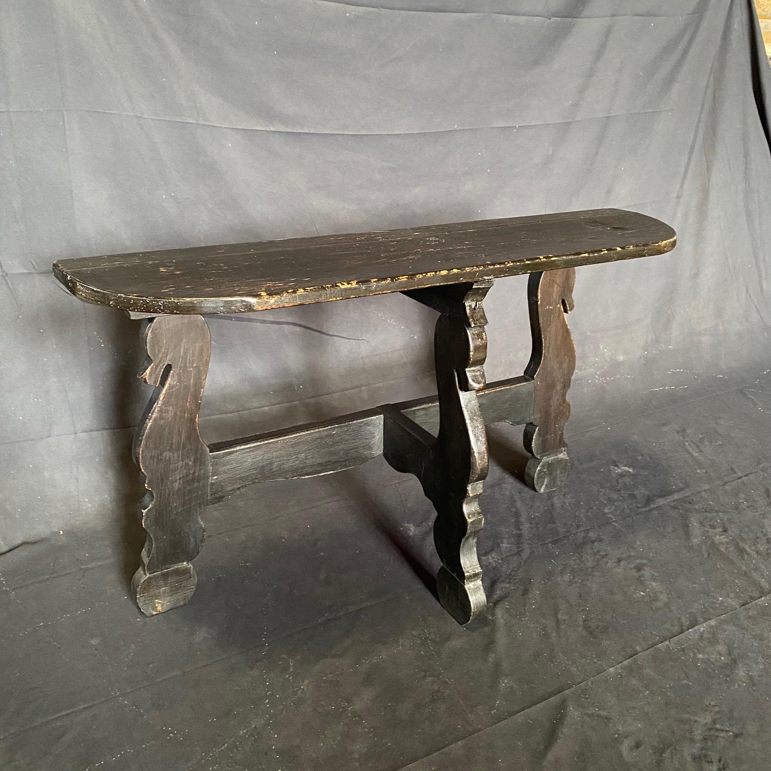 An exceptional pair of 19th century Spanish Baroque demilune tables or consoles in ebony painted walnut wood with elaborated design and carved figural scroll elements on the supports. The oval tops have lovely rustic rounded edges and are supported