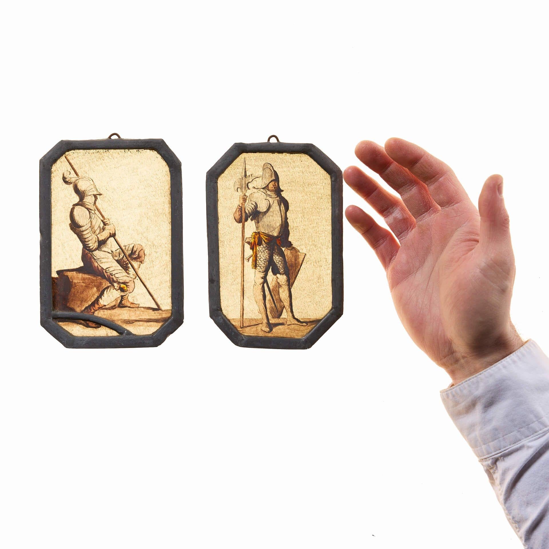 Ein Paar antike Buntglasscheiben mit mittelalterlichen Soldaten. Diese um 1780 entstandenen Glasmalereien haben sich im Laufe der Zeit bewährt; jede einzelne zeigt Präzision, Detailtreue und gute handwerkliche Qualität.

Der eine sitzt, der andere