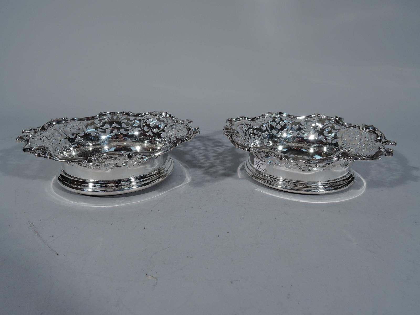 Pair of Victorian sterling silver wine bottle coasters. Made by Howard in New York in 1888. Each: Solid well with engraved armorial. Sides have pierced scrollwork, and rim has applied scrolls and leaves. Mounted to felt-lined wood. Fine pieces by a