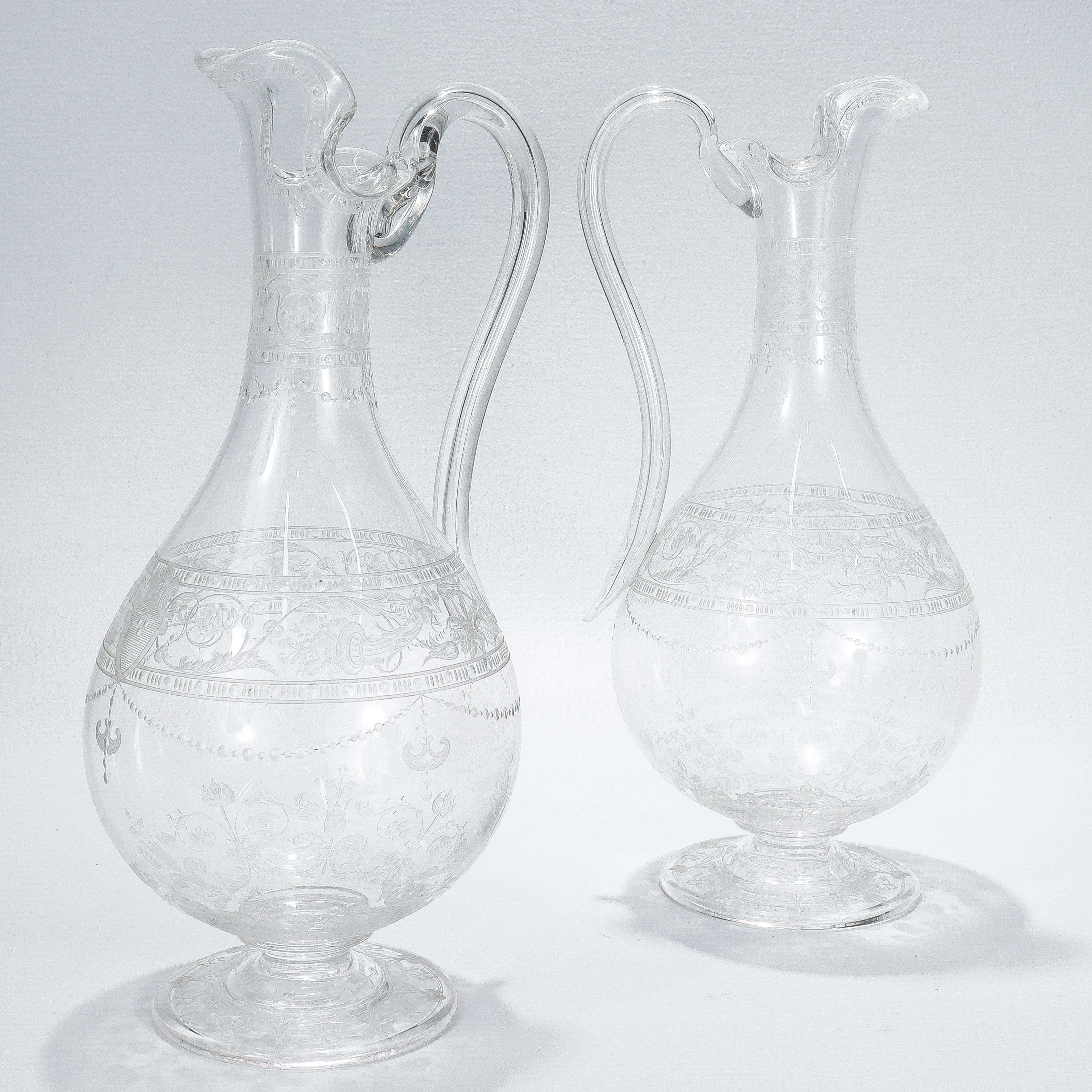A fine pair of antique English etched and engraved glass water pitchers or decanters.

Attributed to Stevens & Williams or Webb.

With engraved & etched designs trelliswork, flowers, and shield devices.

Each with a shaped rim and curved