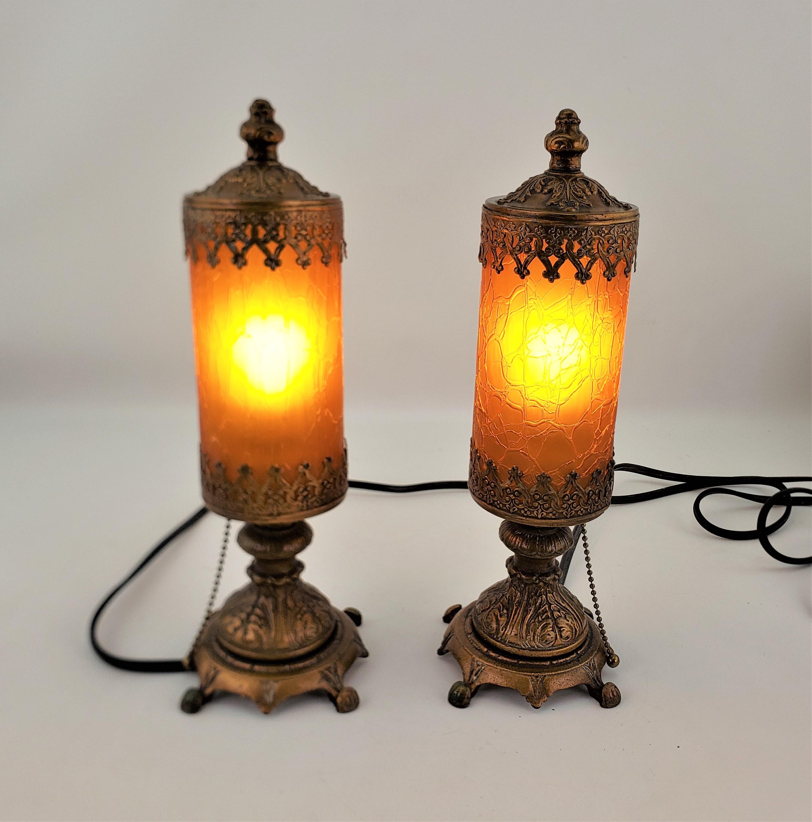 This pair of amber crackle glass accent or boudoir lamps are unsigned, but presumed to have been made in the United States in approximately 1920 in a Victorian period style. The lamps are composed of pressed and patinated metal with ornately