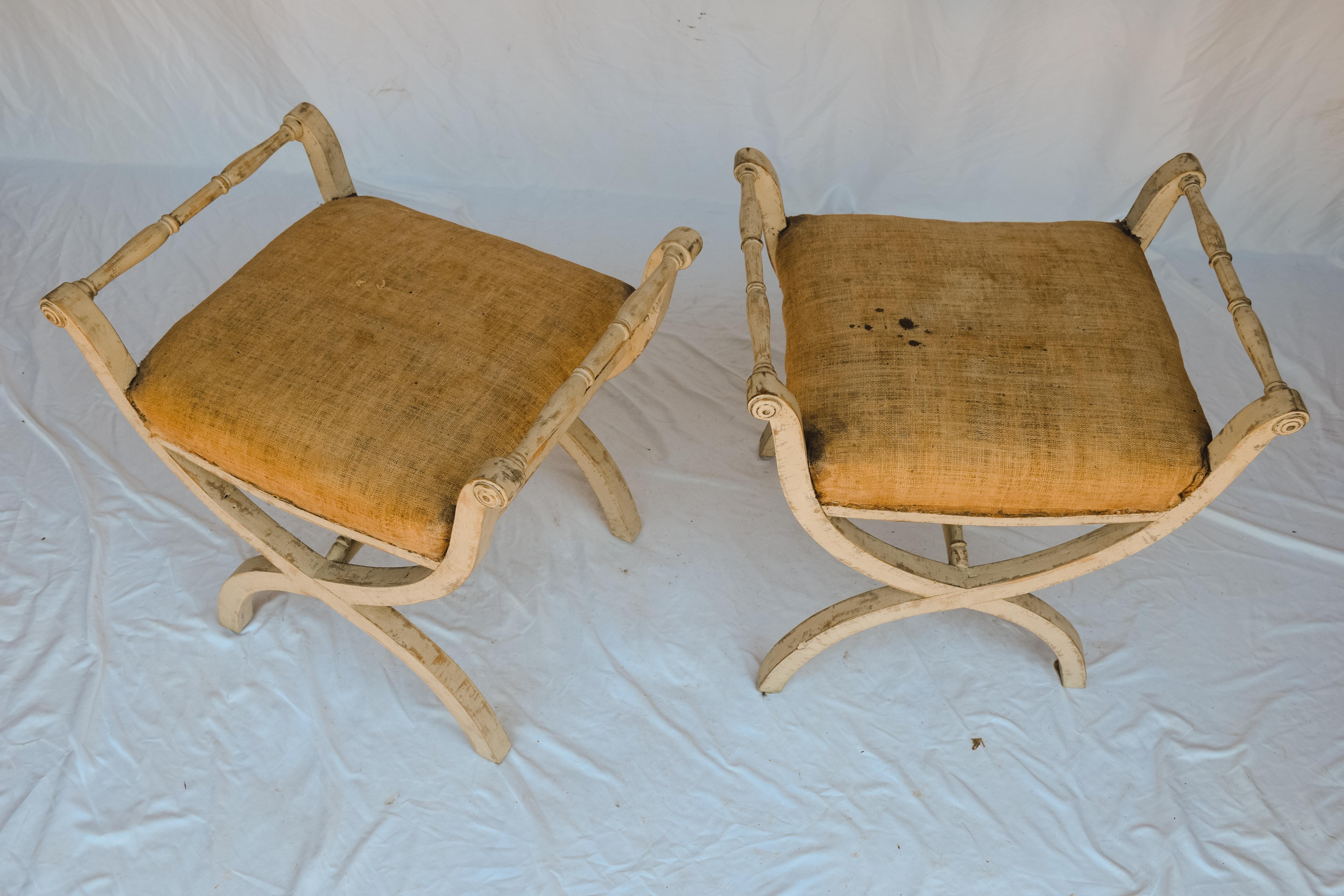 This pair of Antique Swedish Gustavian Stools has two low arms and an x-shaped frame. They have a beautiful aged ivory painted patina and reinforced seats upholstered in their original linen.